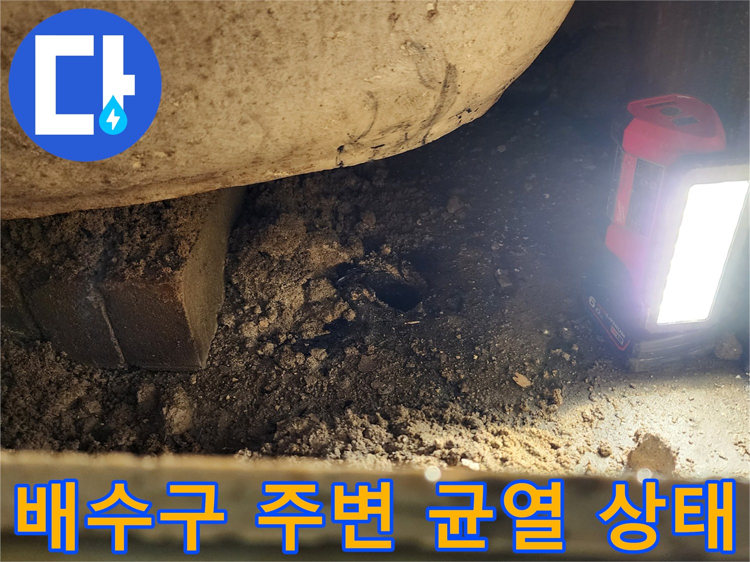 손전등 빛에 드러난-배관 하부의 젖은 토사와 이물질