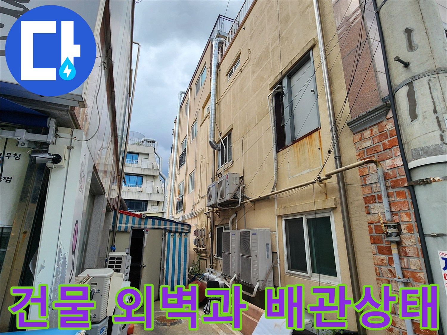 건물 외부 벽면에 설치된 에어컨 실외기와 노후된 배관의 모습입니다.