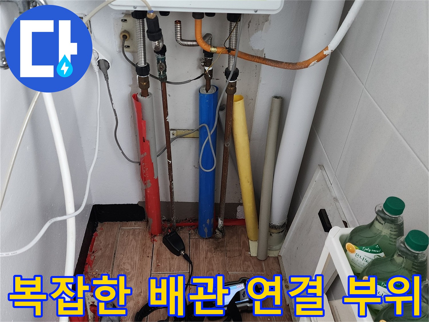 주방 싱크대 하부의 다양한 수도 라인과 보일러 배관의 복합적인 구성 상태를 보여줍니다.