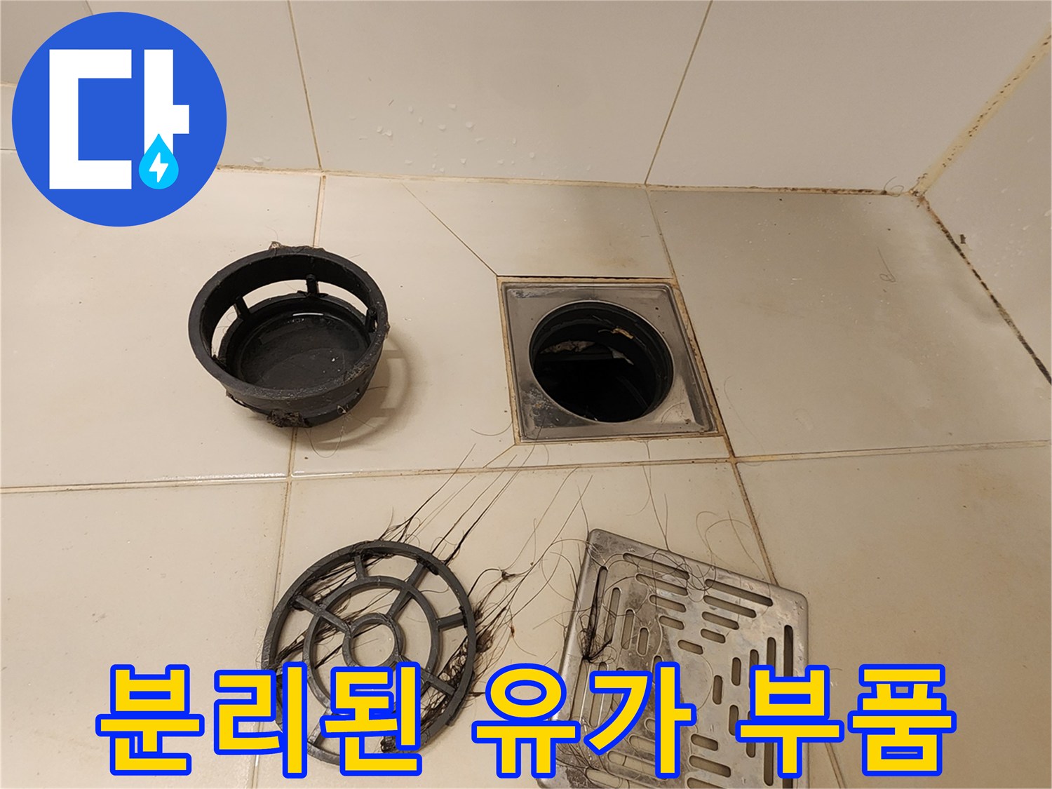 탈거된 배수구 트랩과 덮개가 놓인 욕실 바닥 사진입니다.