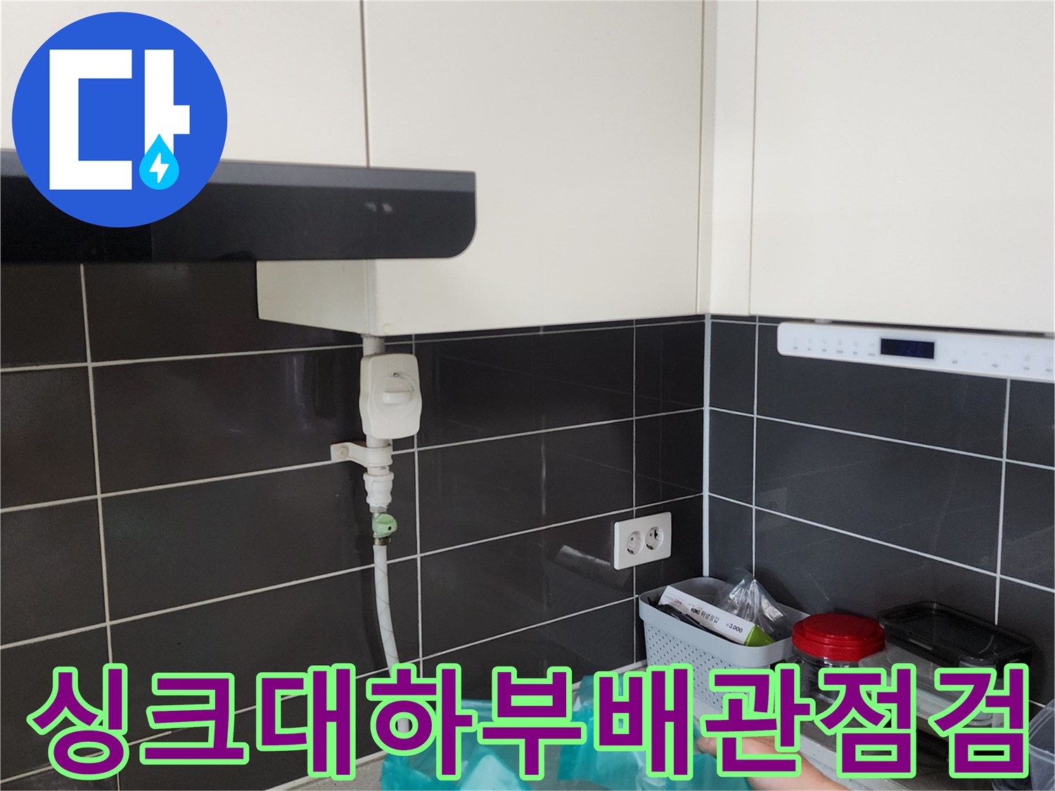 주방 싱크대 하부장 아래쪽의 수도 배관과 전기 콘센트 주변 상태를 확인하는 모습입니다.