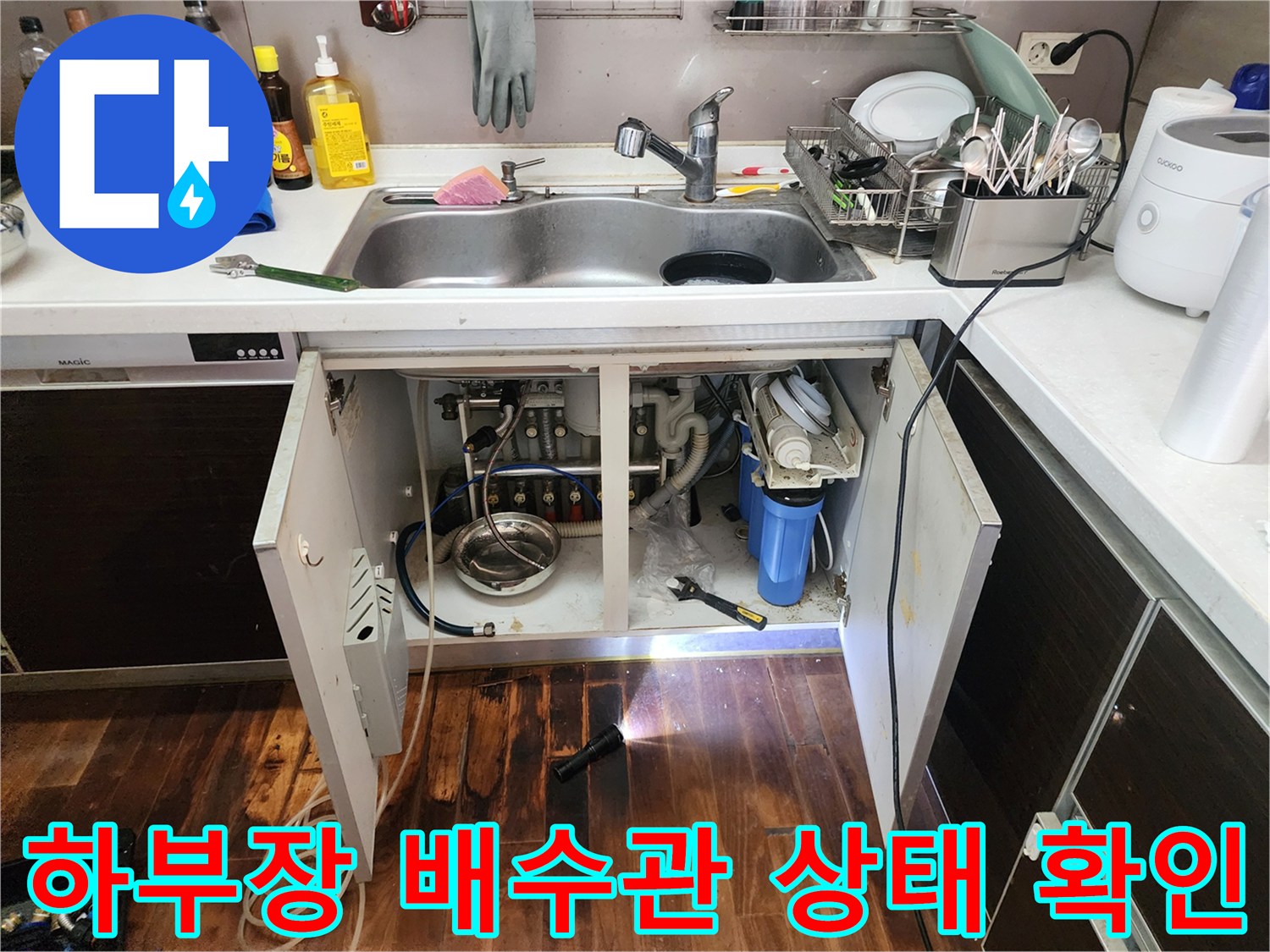 손전등 빛을 이용해 싱크대 하부 배수 호스 및 연결 부위를 정밀하게 탐색하는 장면