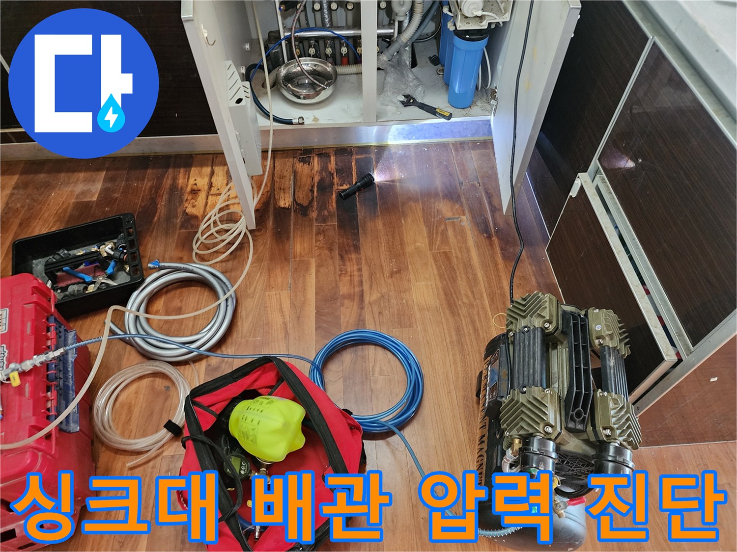 콤프레샤와 호스를 연결하여 싱크대 하부 배관에 공기압을 가하는 장면