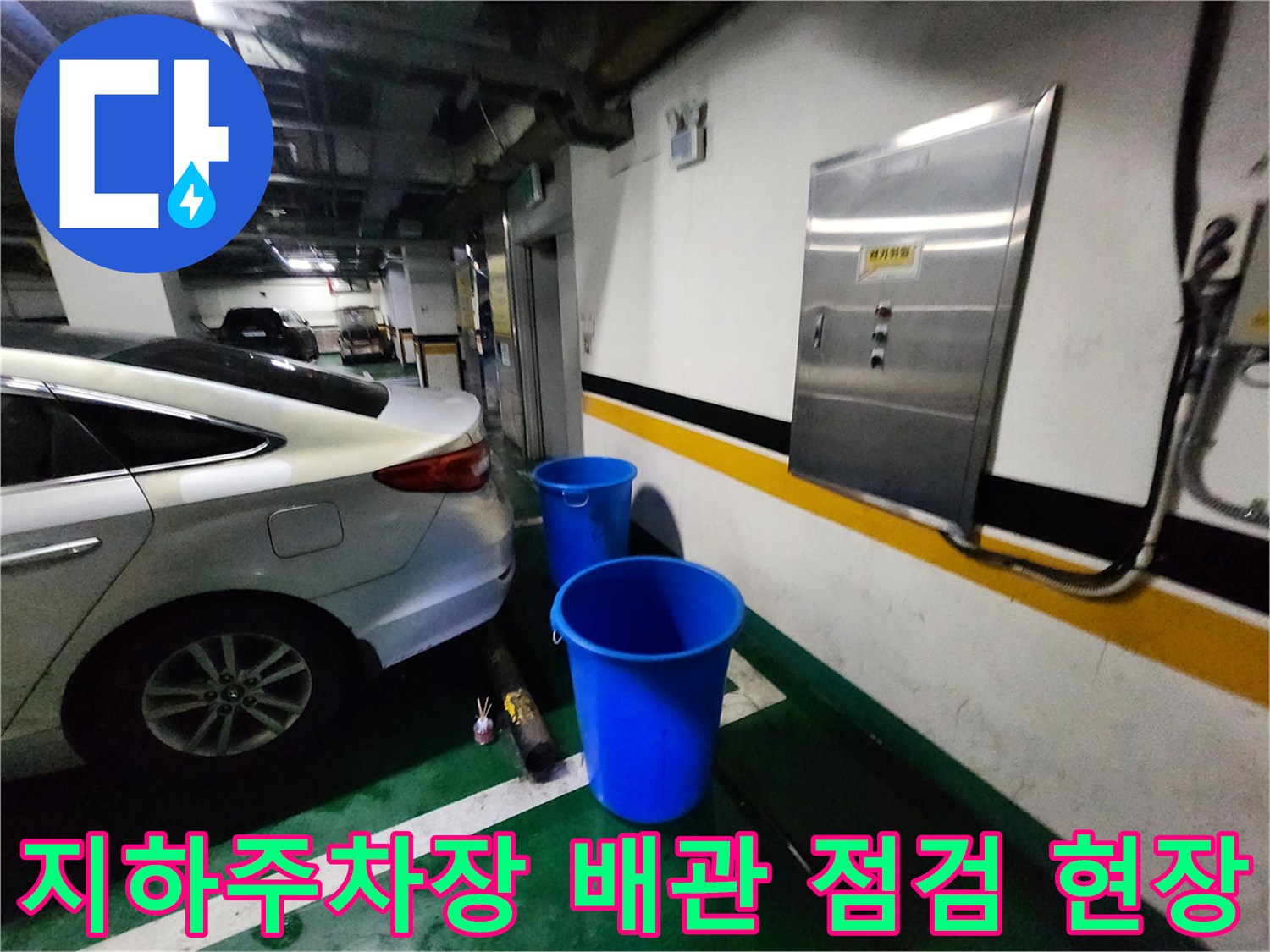 지하 주차장 벽면 배관 근처에 파란색 양동이가 놓여 있는 모습