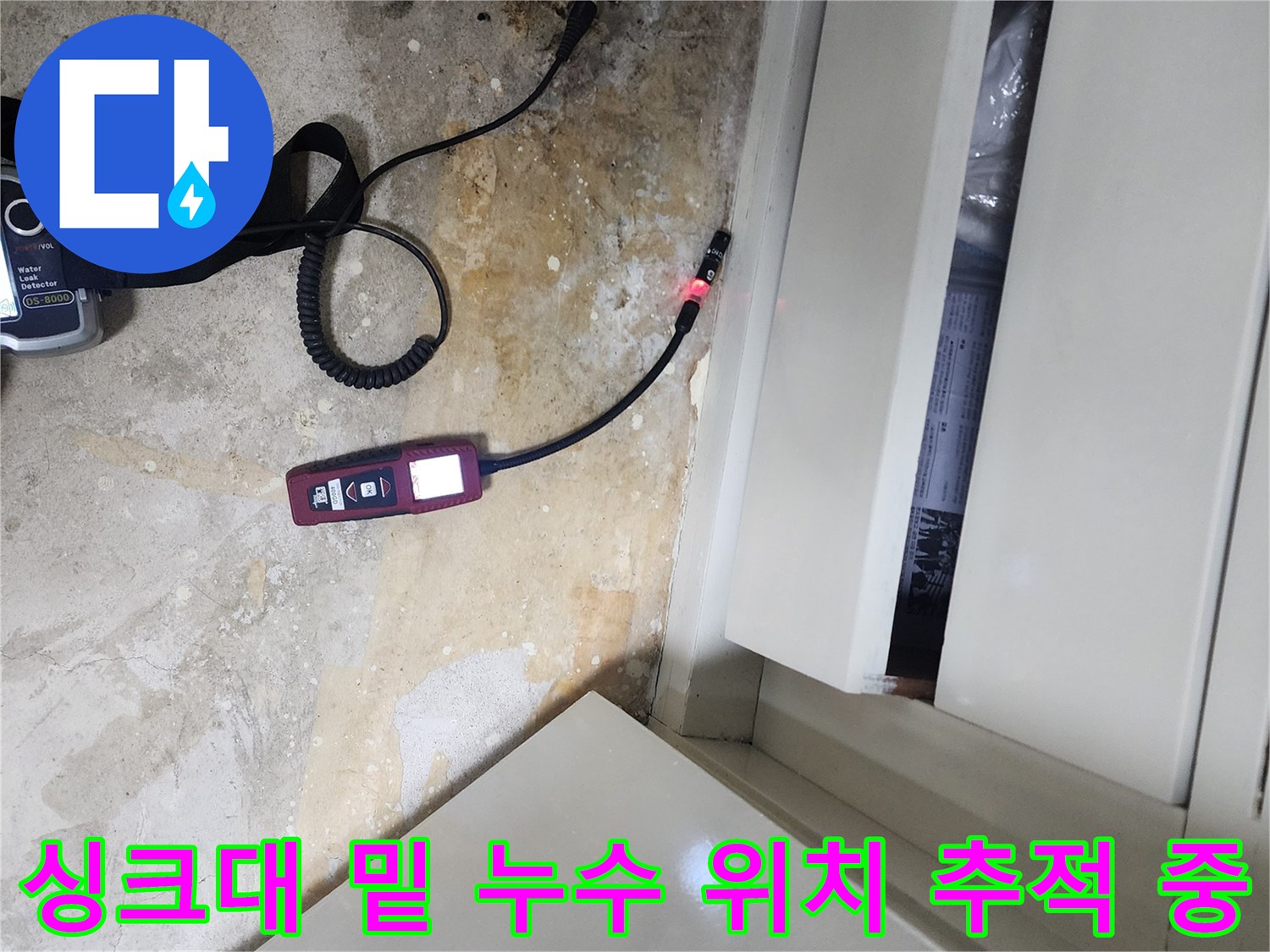 싱크대 하부장 아래 오염된 바닥 부근에서 가스 탐지기로 누수원을 찾는 모습입니다