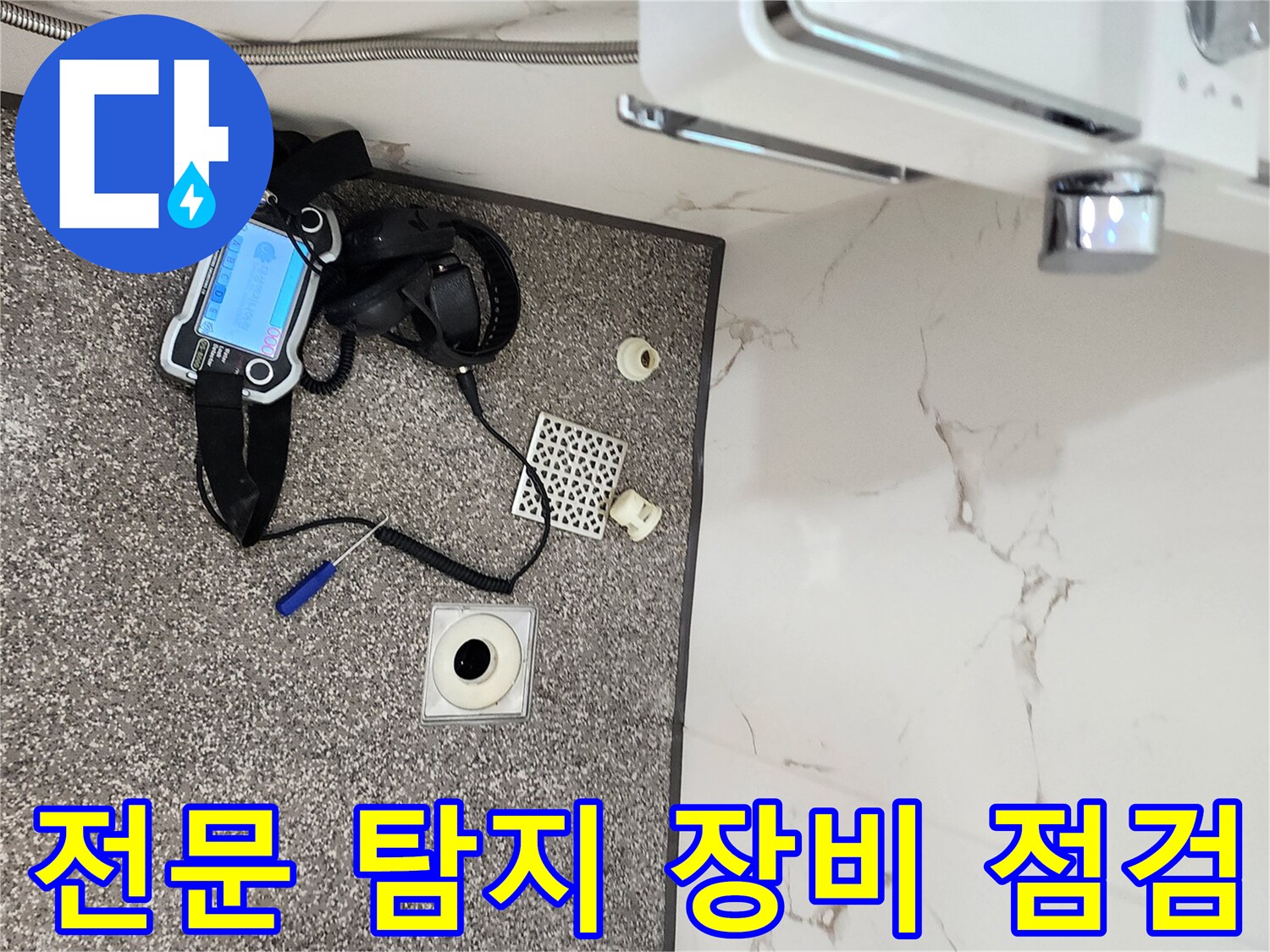 욕실 바닥에 놓인 가스 탐지기와 배수구 부속품 사진