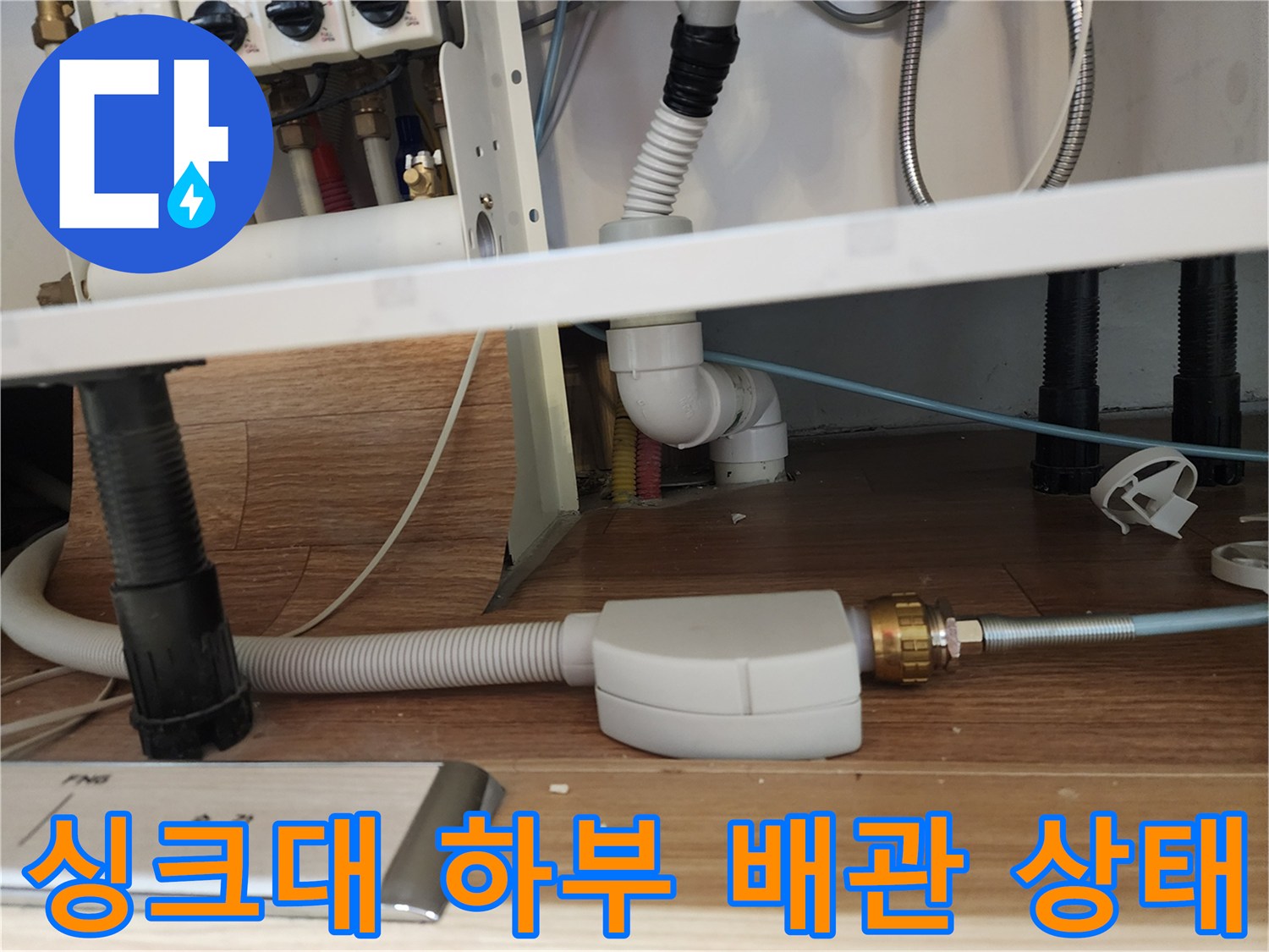 주방 싱크대 아래쪽의 복잡한 배관 연결 부위와 호스 모습