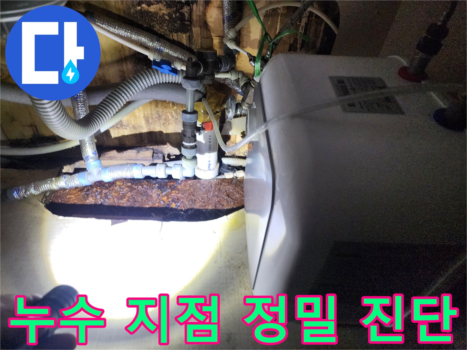 손전등으로 비춘 온수기 하단 배관 연결부의 누수 흔적