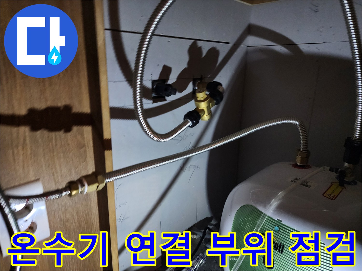 주방 하부장 내 전기 온수기와 금속 급수 배관의 근접 사진