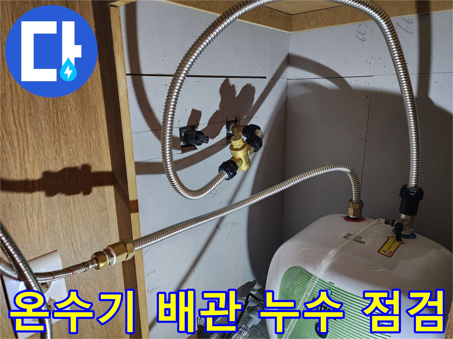 주방 하부장 내 전기 온수기와 연결된 금속 호스의 상태를 확인하는 모습