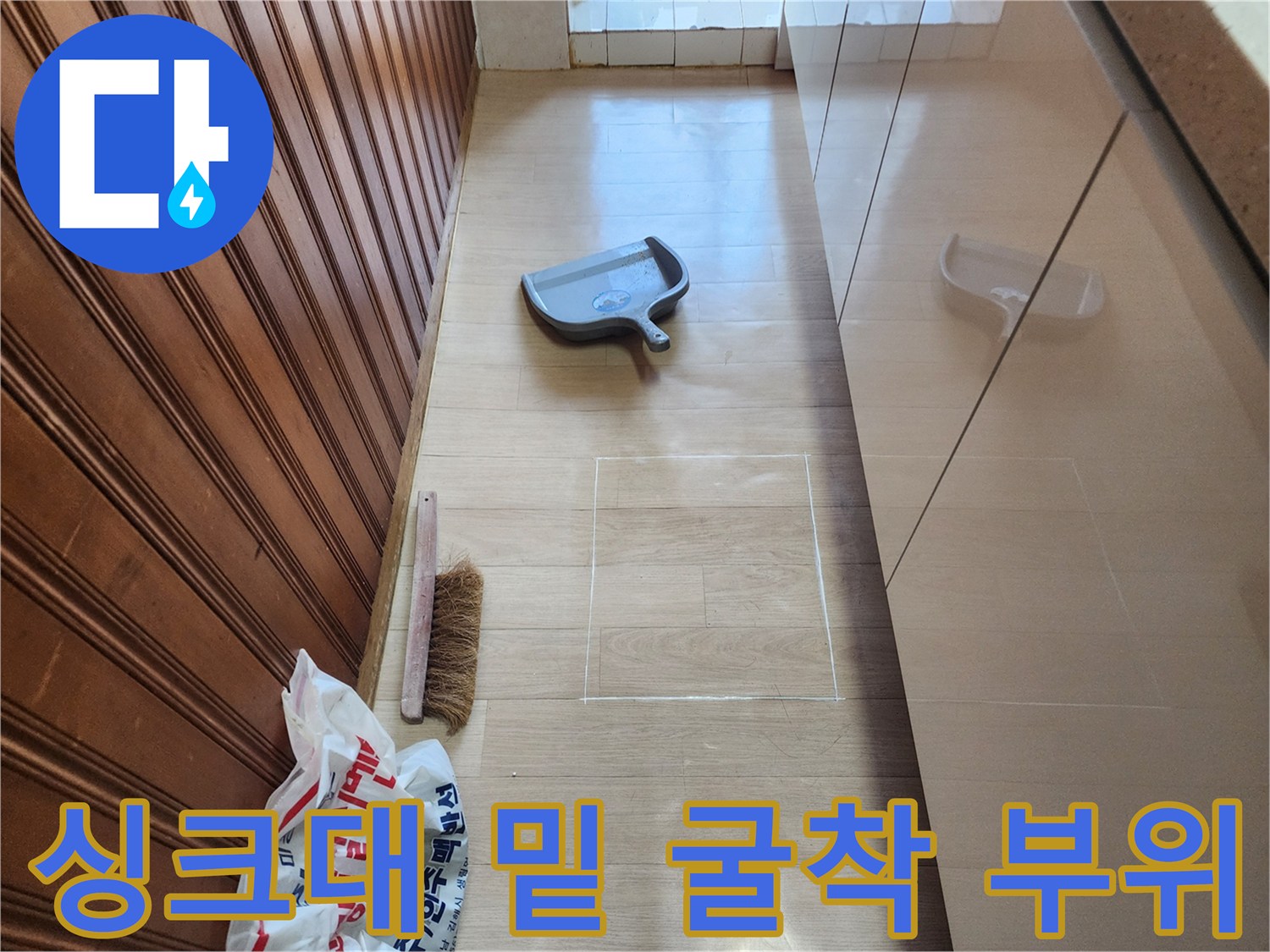 주방 싱크대 하단 마루를 제거하여 배관을 노출시킨 공사 현장입니다.