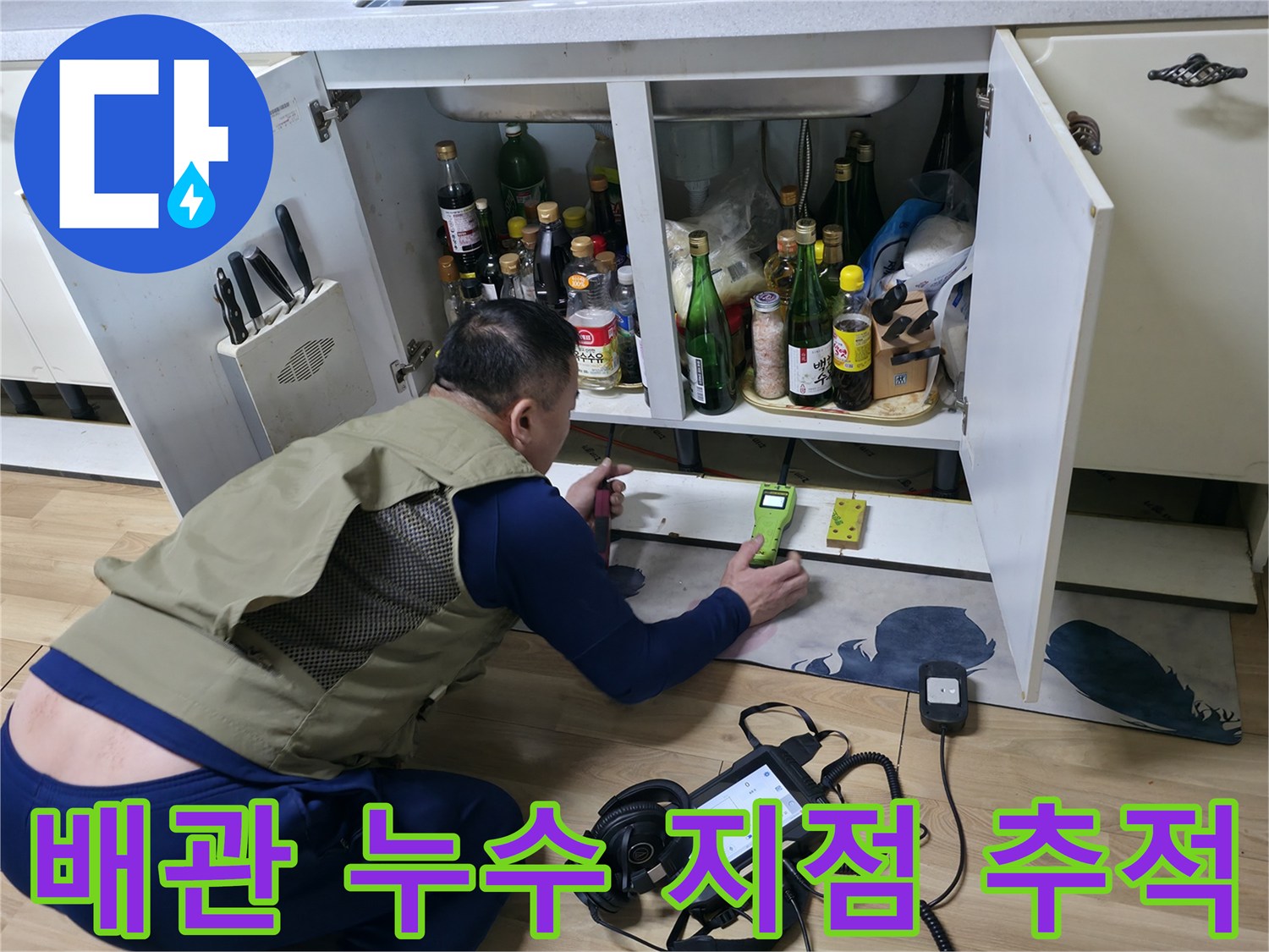 주방 싱크대 아래 공간에서 가스식 탐지기로 배관의 미세한 누수를 찾는 중입니다.
