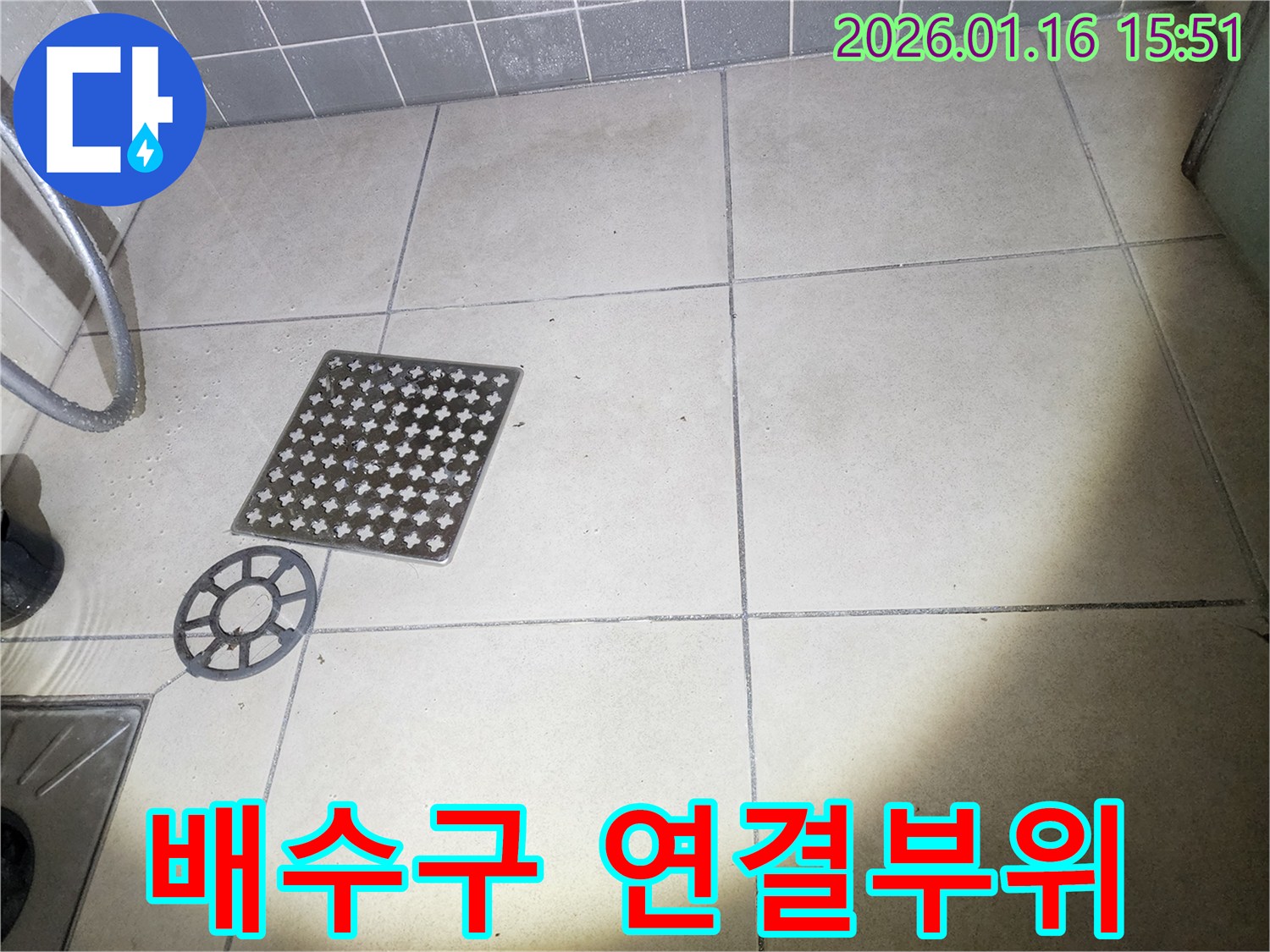 이 이미지는-욕실 바닥의-배수구 커버를-제거하고-연결 부위의-누수 여부를-확인하는-장면을 보여줍니다