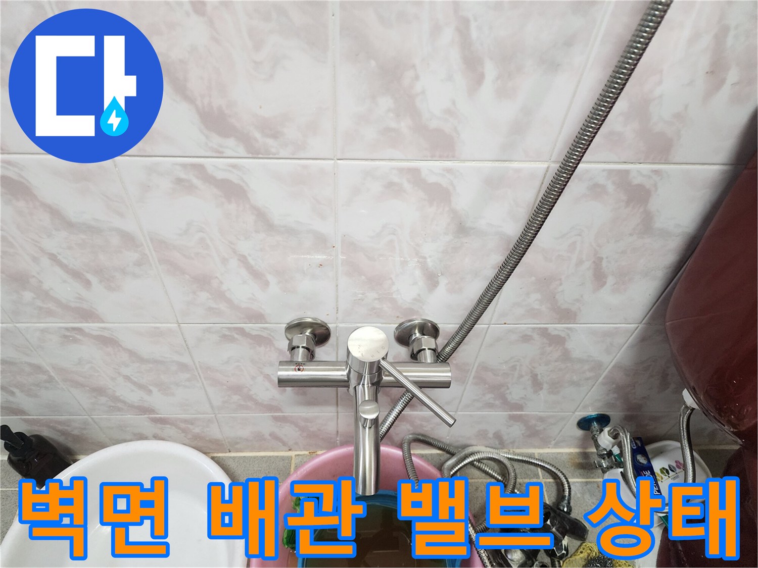 타일 벽면에 설치된 은색 수도 밸브와 유연한 금속 호스의 연결 부위