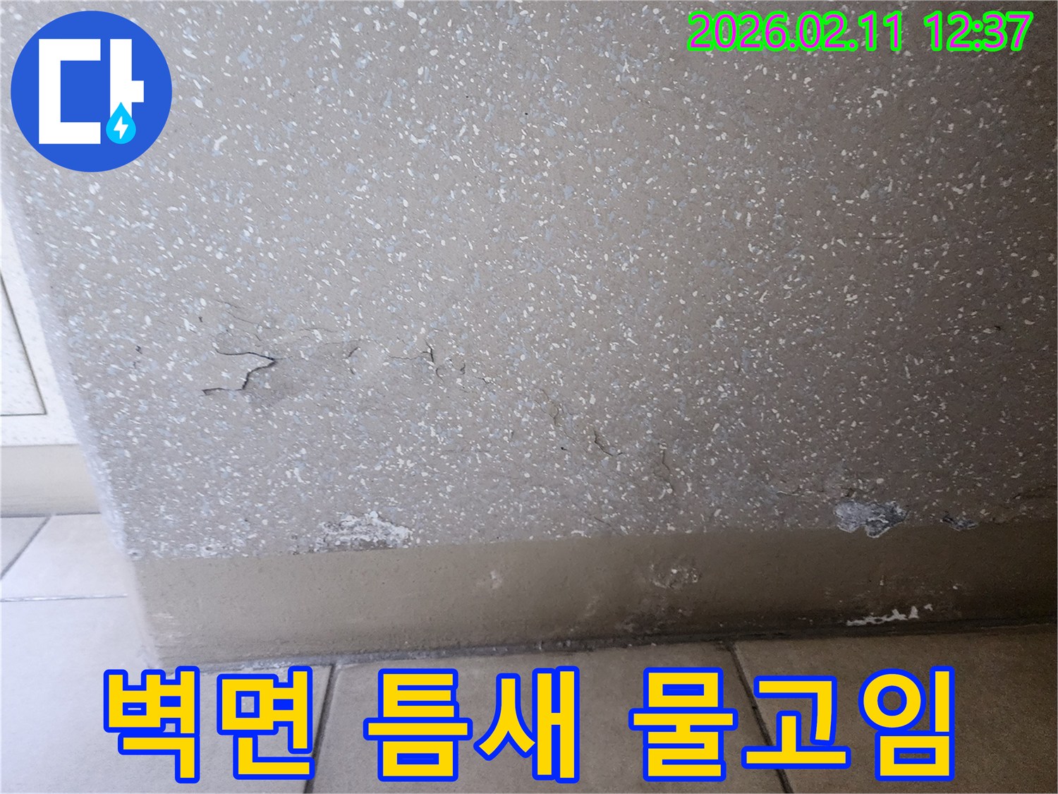 이 사진은 벽면 하단에 물이 고여 있고-벽면 틈새로 물이 스며들어 손상된 누수 현장을 보여줍니다.