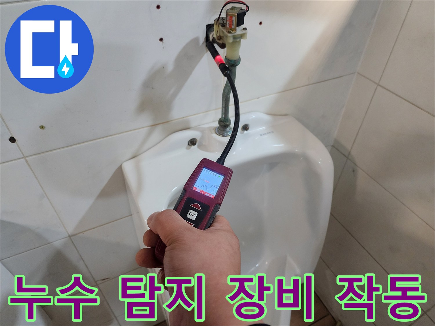 손에 든 휴대용 가스 탐지기로 타일 틈새의 누수 반응을 살피는 현장 사진입니다.