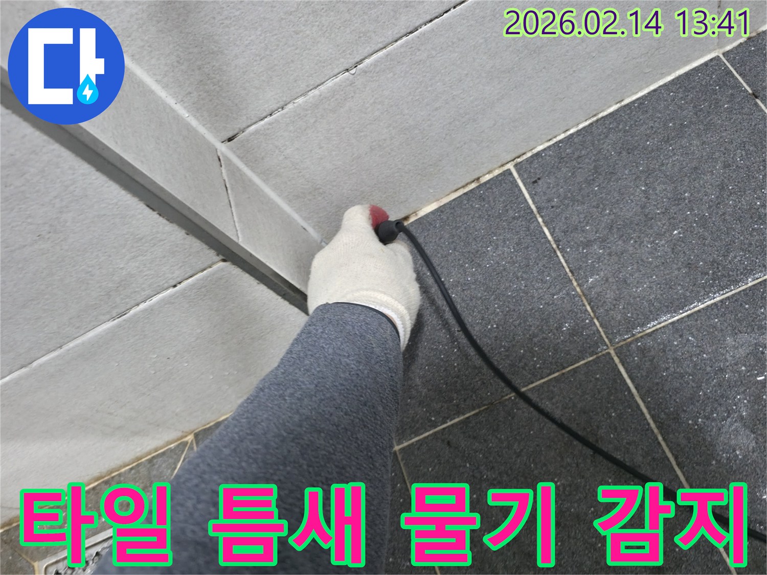 누수 엔지니어가-작업 장갑을 끼고-누수 탐지 장비로-화장실 타일 틈새의-미세한 물기를 감지하는 장면입니다.