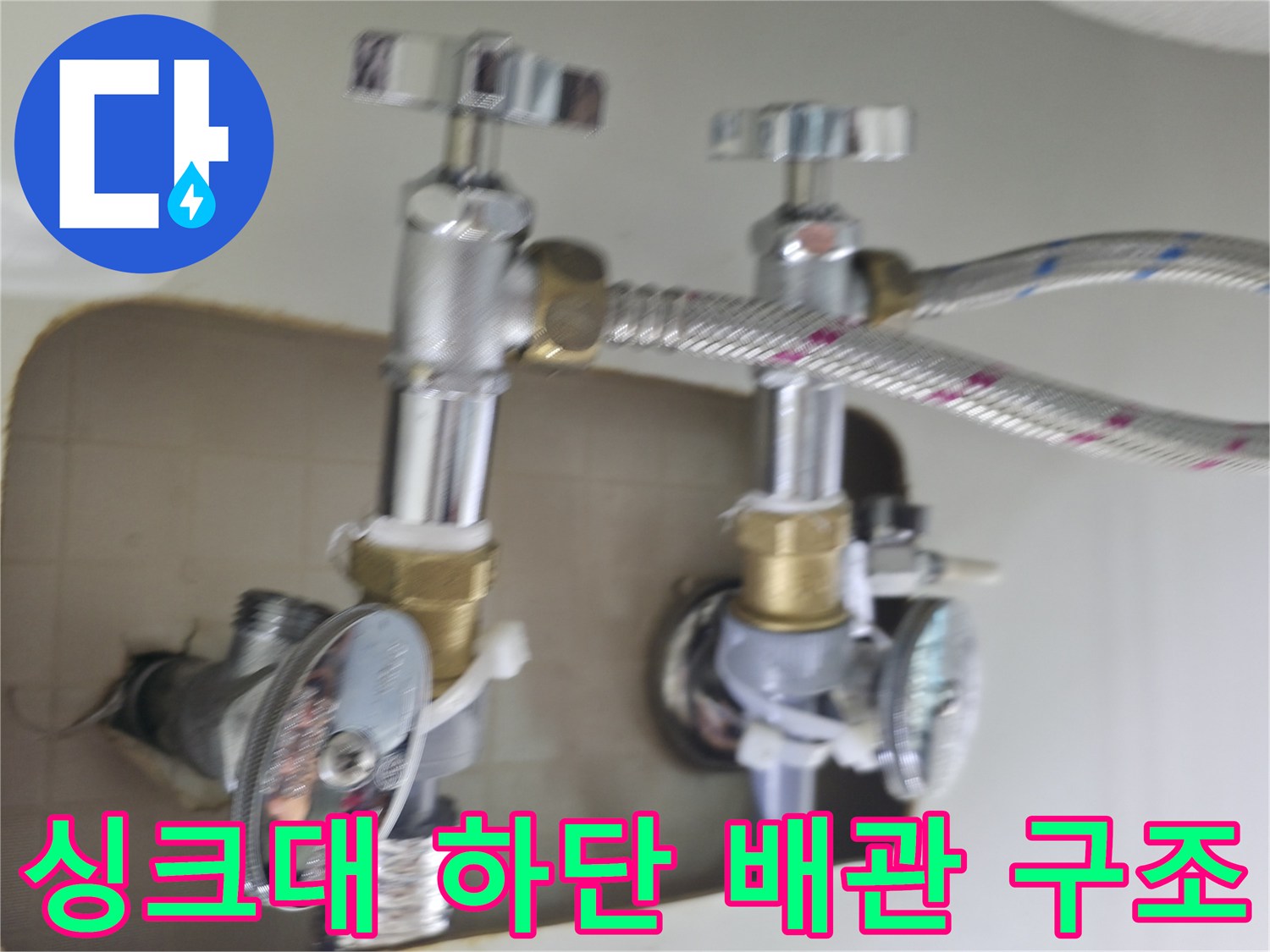주방 싱크대 아래 설치된 수도 밸브와 은색 주름관의 연결 부위입니다.