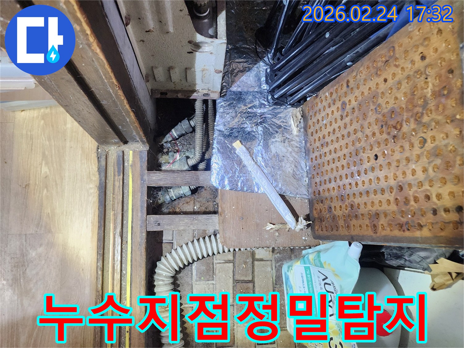 물건들로 가득 찬-좁은 공간 아래에서-누수 지점을 찾아내기 위해-조사하는 장면입니다