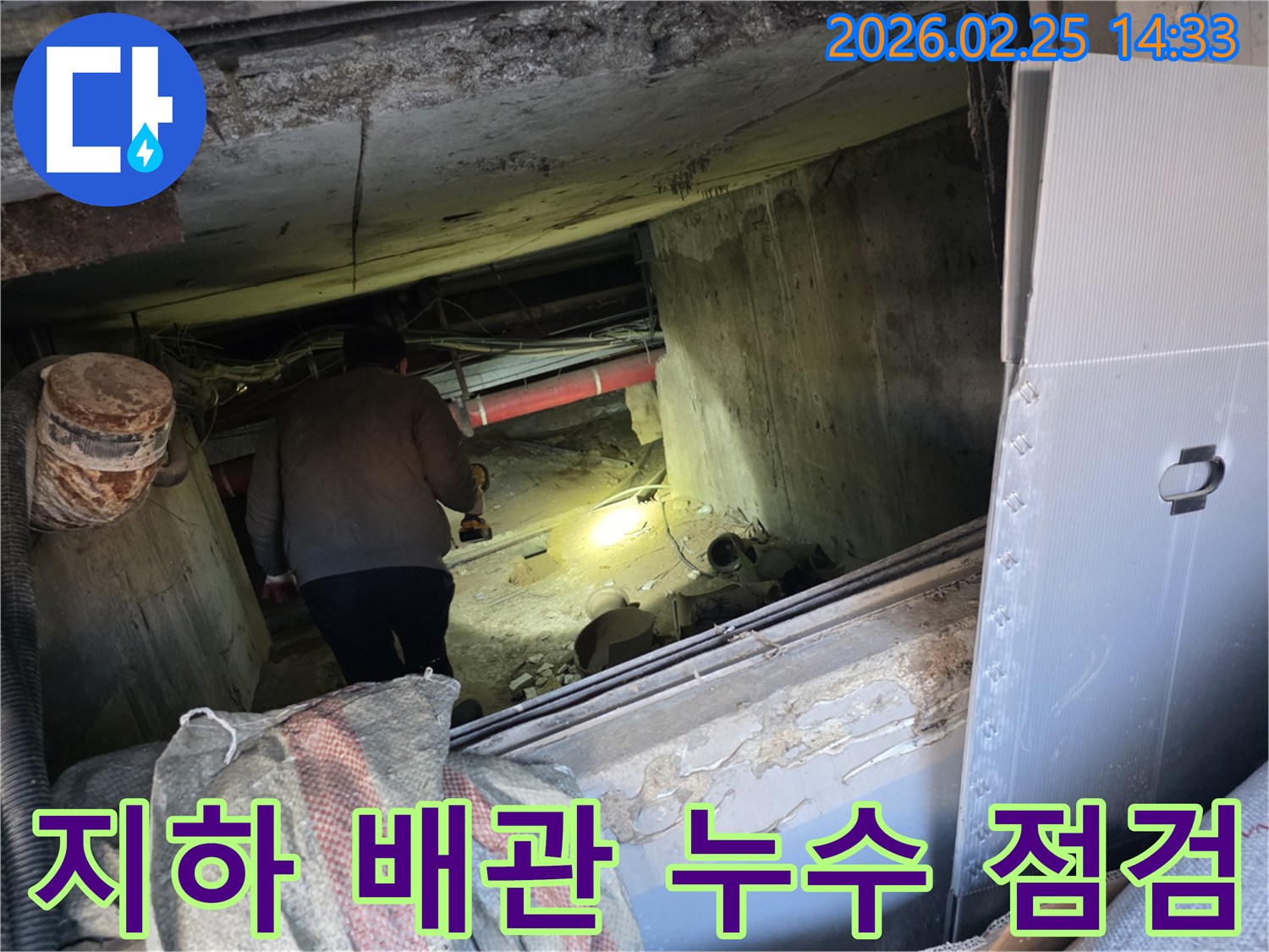 누수 전문 엔지니어가-어두운 지하 공간에서-손전등을 비춰-복잡하게 얽힌 배관들을-하나하나 면밀히 살펴보며-누수 흔적을 찾는 모습입니다.