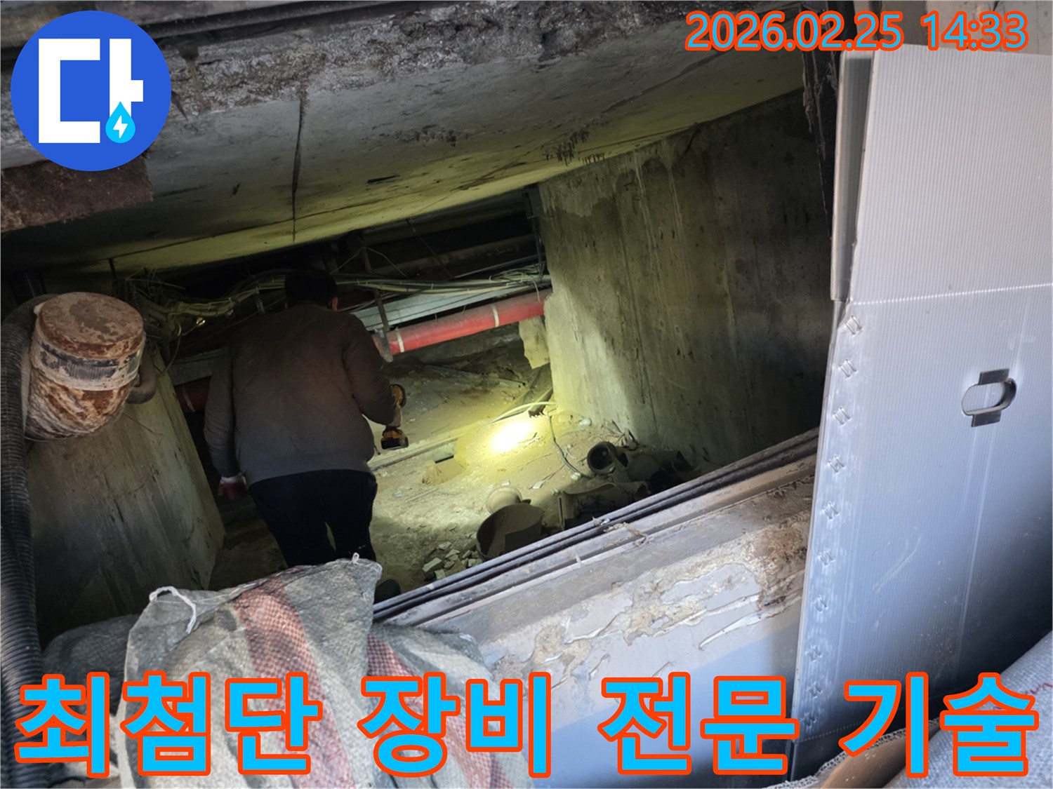 누수 전문 엔지니어가-어둡고 좁은 공간에서-손전등을 비춰가며-최첨단 장비와 전문 기술을 활용하여-숨겨진 누수 문제를-해결하기 위해 탐지하는 모습입니다.
