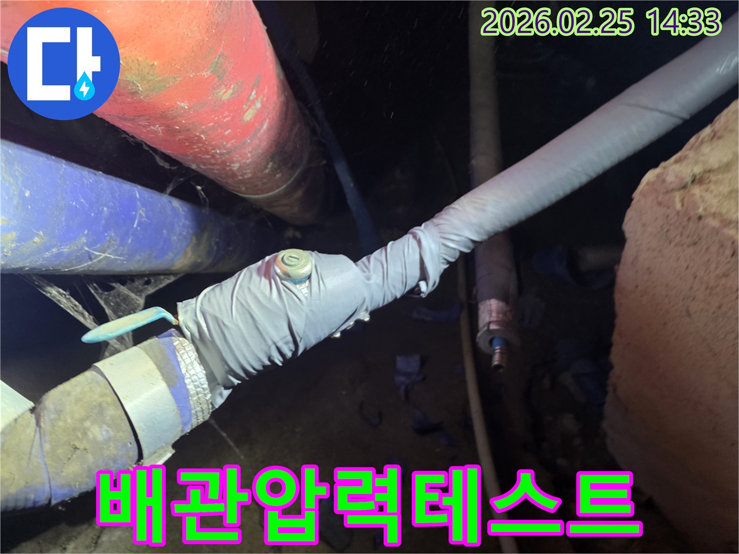 어두운 공간에서 배관 연결부에 압력 테스트 장비를 설치하여-미세한 누수 지점을 찾아내는 정밀 작업입니다