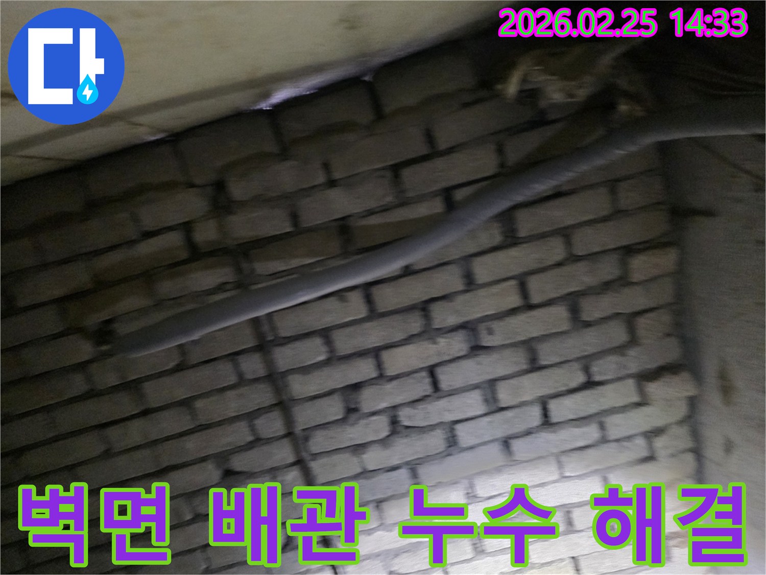 어두운 벽돌 벽면을 배경으로-단열재로 감싸인 배관과-다른 배선이 누수 여부를-확인하기 위해 촬영된 현장 이미지입니다.
