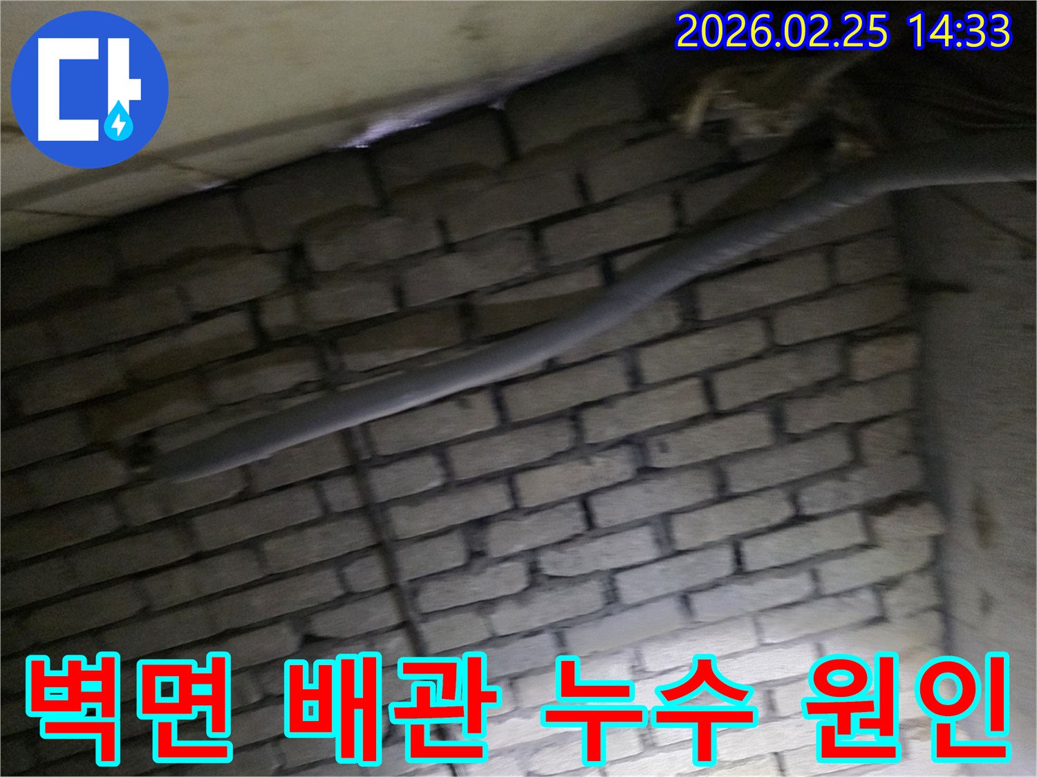 어두운 벽돌 벽면을 배경으로-단열재로 감싸인 배관과-다른 배선이 누수 여부를-확인하기 위해 촬영된 현장 이미지입니다.