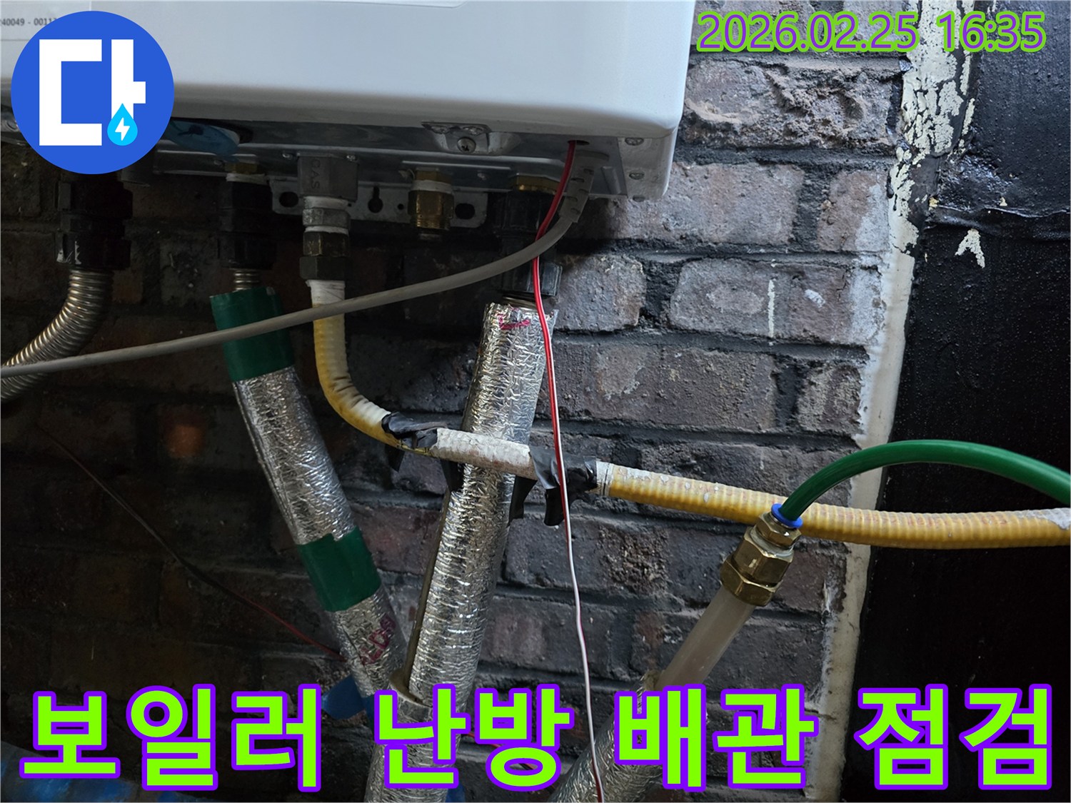 이 이미지는-벽에 설치된-보일러 하단부의-난방 배관과-온수 배관-그리고-전선이-연결된-모습을-보여주며-난방 누수 여부를-확인하기 위한-정밀한 점검이-진행되고-있음을-암시합니다.