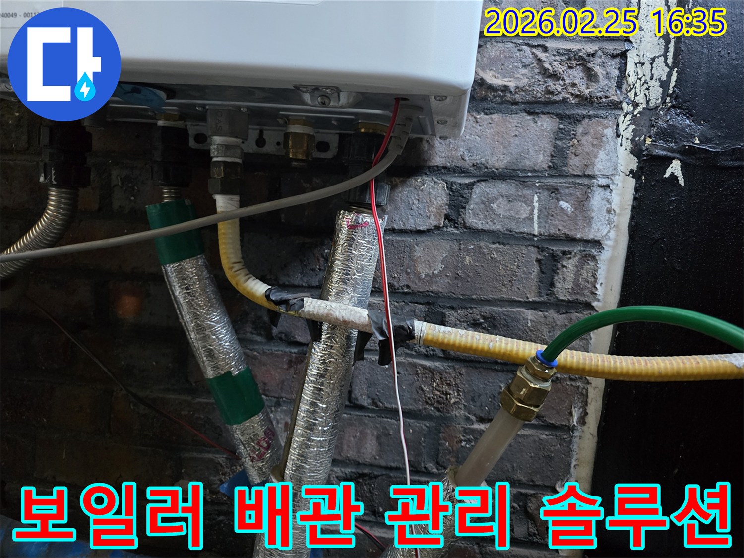 이 이미지는-벽에 설치된-보일러 하단부의-복잡한 배관 연결부와-전선-그리고-은색 단열재로-감싸진-파이프들을-보여주며-누수 방지를 위한-배관 관리 솔루션이-필요함을-암시합니다.