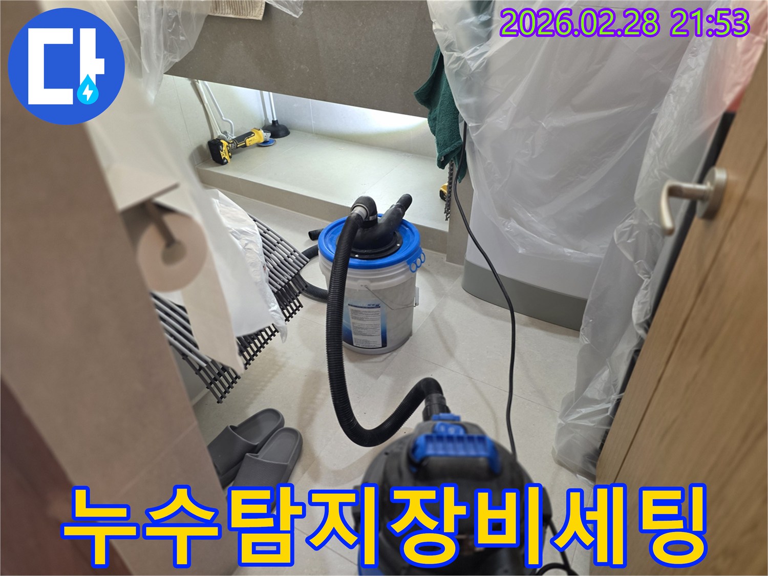 이 이미지는 누수 탐지 작업을 위해-주변을 비닐로 꼼꼼히 보양하고-습식 청소기와 조명 등-필요한 장비들을 세팅하는 현장을 보여줍니다.
