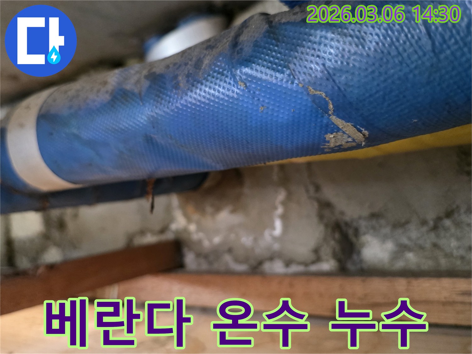 아파트 베란다 하부-파란색 온수 배관과-젖은 콘크리트 벽면-그리고 나무 지지대를-꼼꼼히 점검하는 모습
