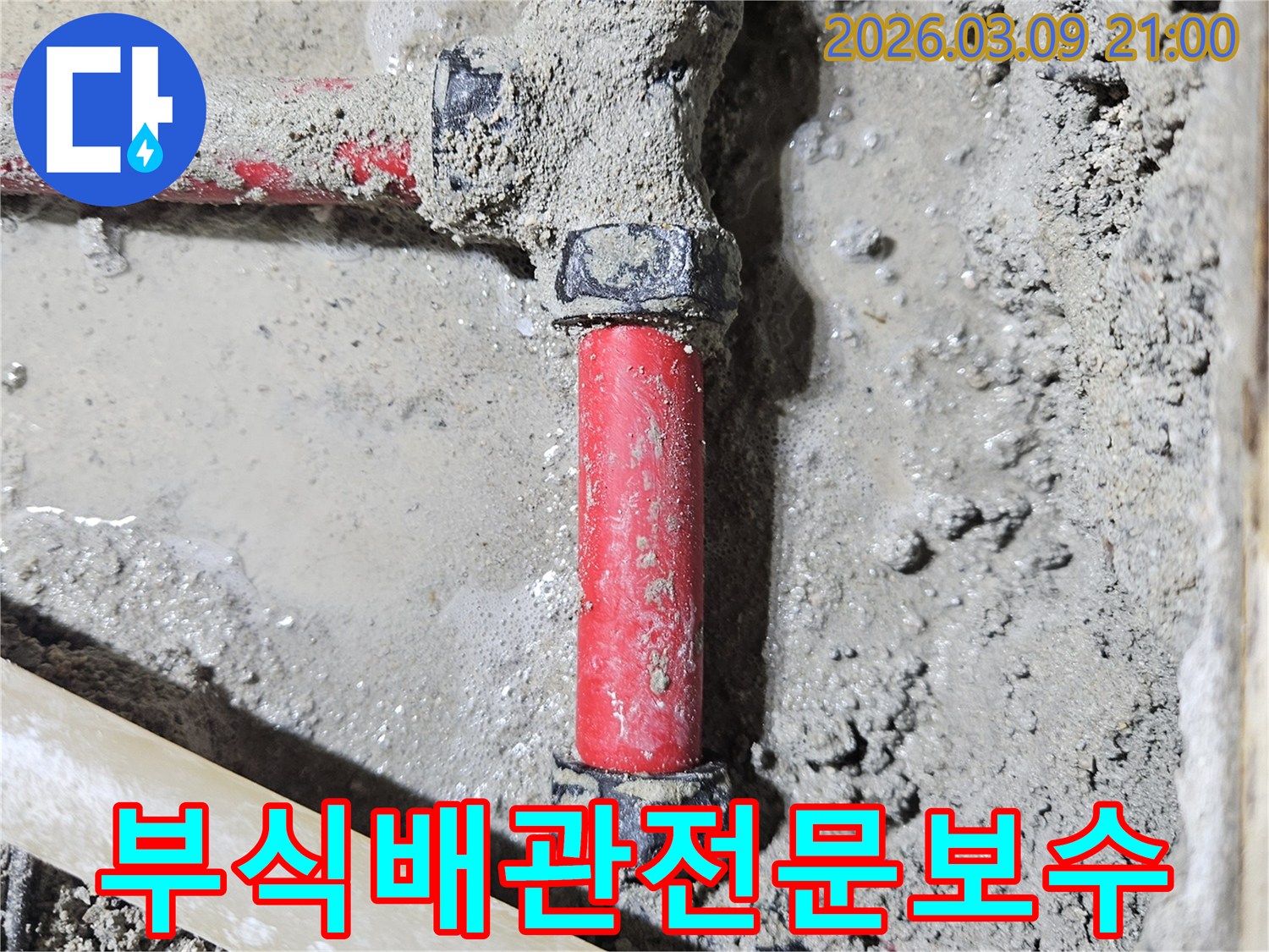 젖은 시멘트 바닥에-매립된 빨간색 부식된 배관의-누수 지점을-새로운 배관으로-전문적으로 보수한-모습입니다