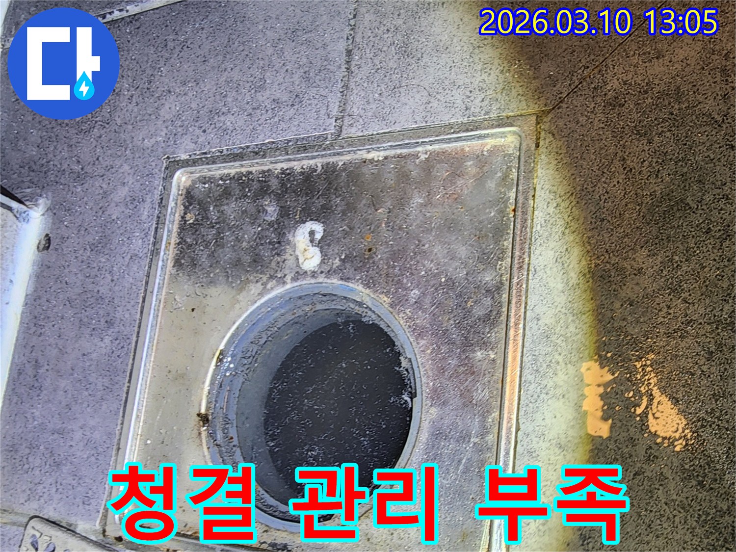 누수 엔지니어가 바닥 배수구 덮개를 열고-주변의 청결 상태와 관리 부족으로 인한 문제점을 진단하는 모습입니다