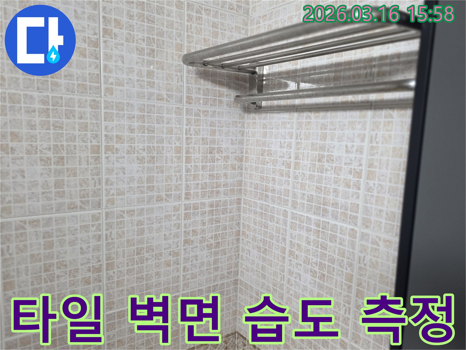 빌라 욕실의 타일 벽면에-누수 엔지니어가-습도 측정 장비를-사용하여-누수 여부를-진단하는 모습입니다.