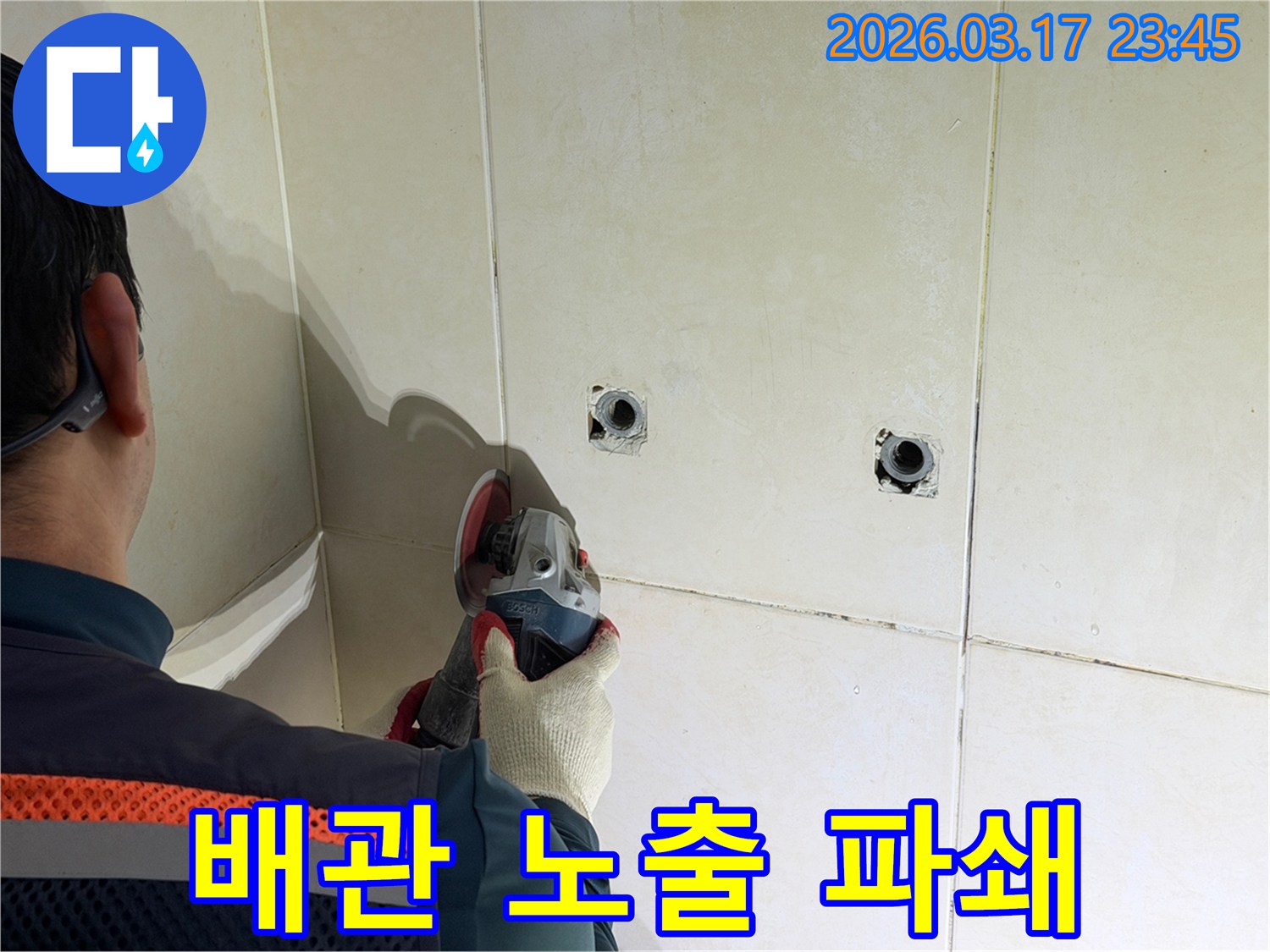 누수된 배관을-노출시키기 위해-전문가가-타일 벽면을-그라인더로-조심스럽게-파쇄하고-있습니다