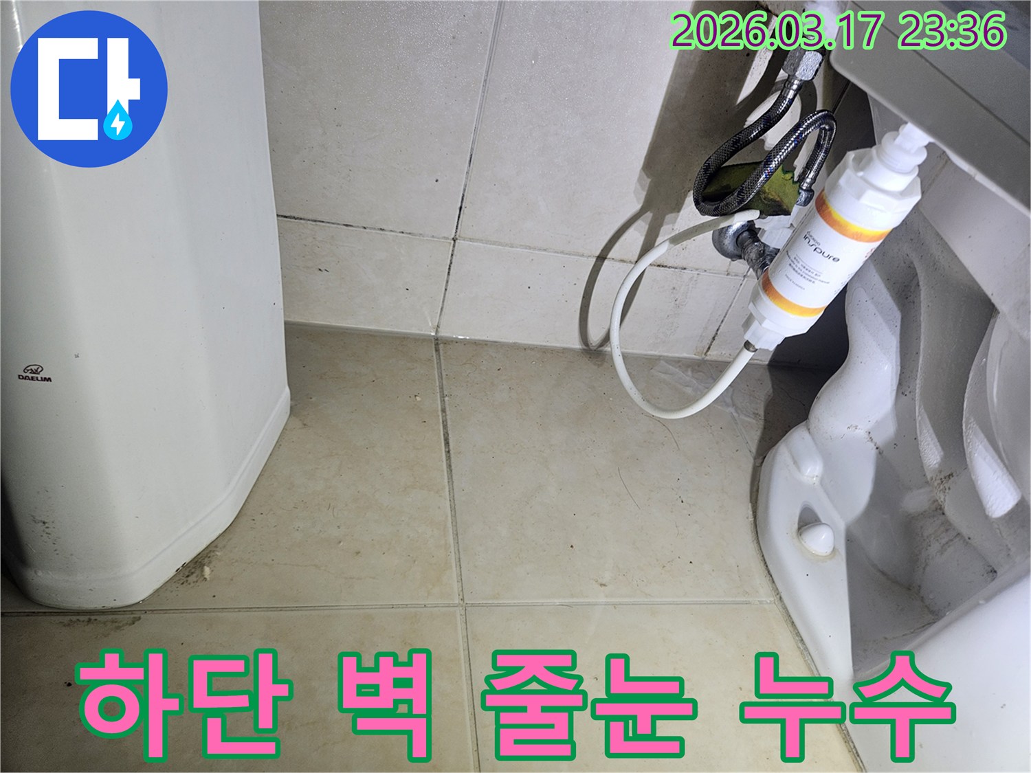 이 이미지는-욕실 벽면 하단 타일의 줄눈에-물이 스며들어-젖어있고-오염된 상태를 보여줍니다.