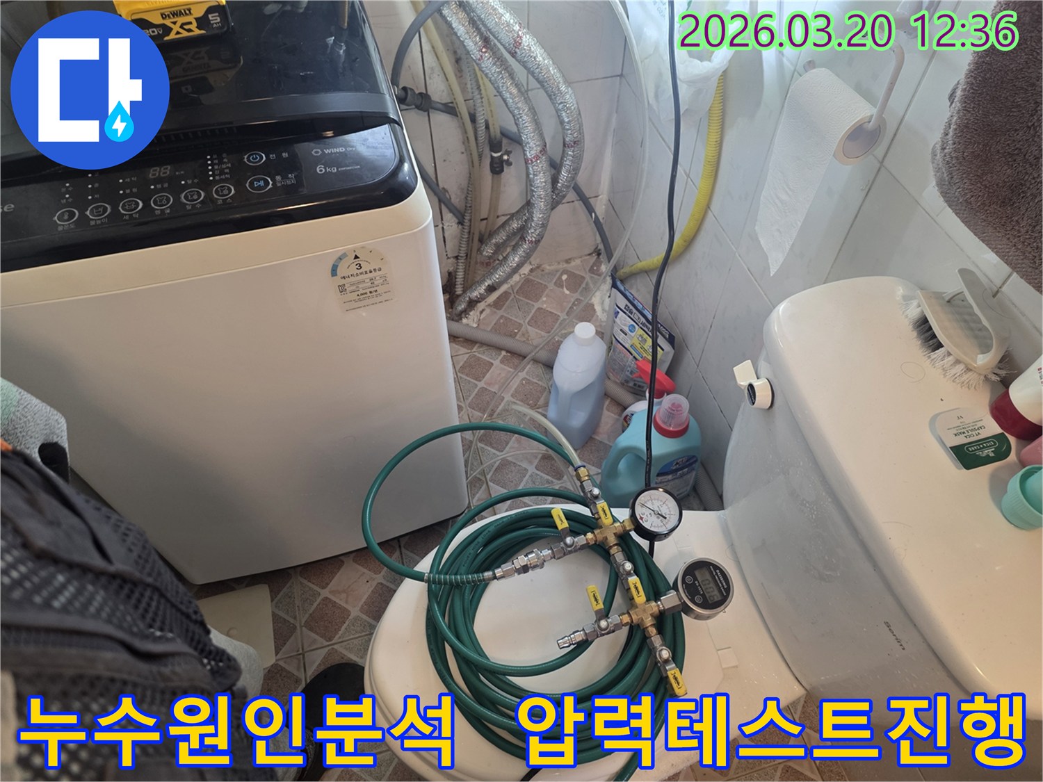 누수 엔지니어가 화장실 변기 위에 놓인-초록색 호스와 압력 게이지를 연결하여-배관의 누수 여부를 정밀하게 확인하고 있습니다