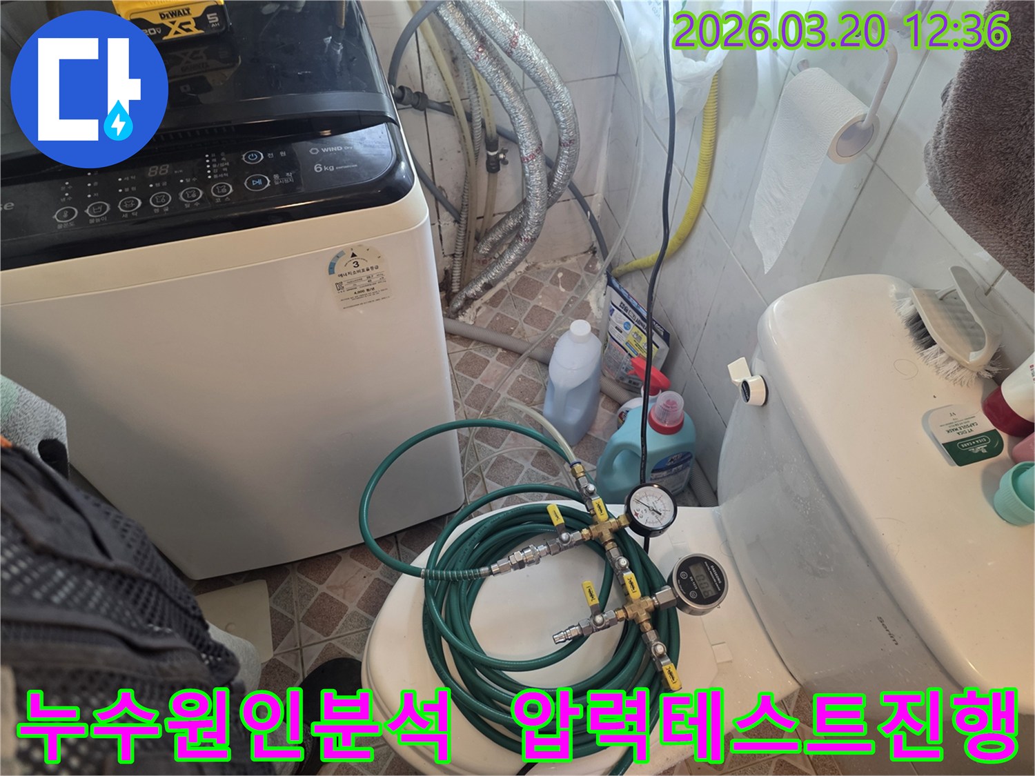 누수 엔지니어가 화장실 변기 위에 놓인-초록색 호스와 압력 게이지를 연결하여-배관의 누수 여부를 정밀하게 확인하고 있습니다