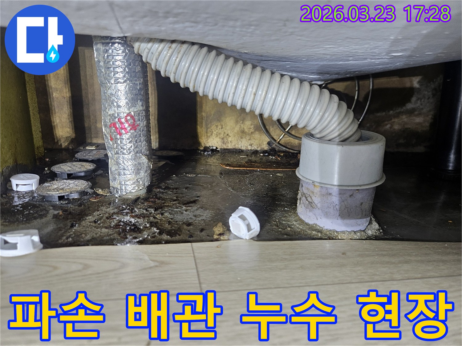 이 이미지는 파손된 배관에서 발생한 누수로 인해 바닥이 심하게 오염되고 물이 고인 현장을 보여주며-즉각적인 수리가 필요합니다.