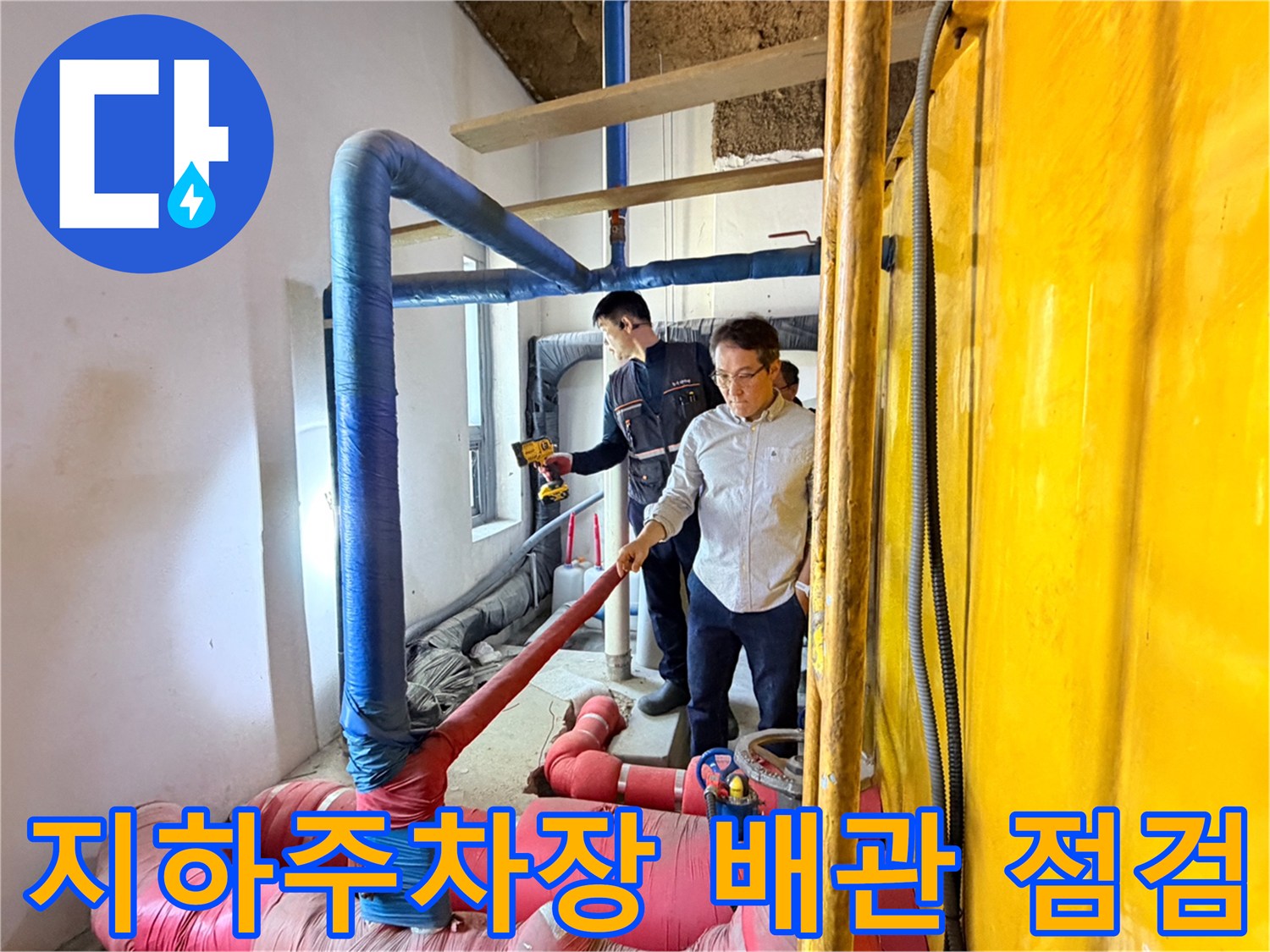 지하 주차장 내부의 파란색과 분홍색 보온재가 씌워진 배관을 엔지니어가 확인하고 있습니다.