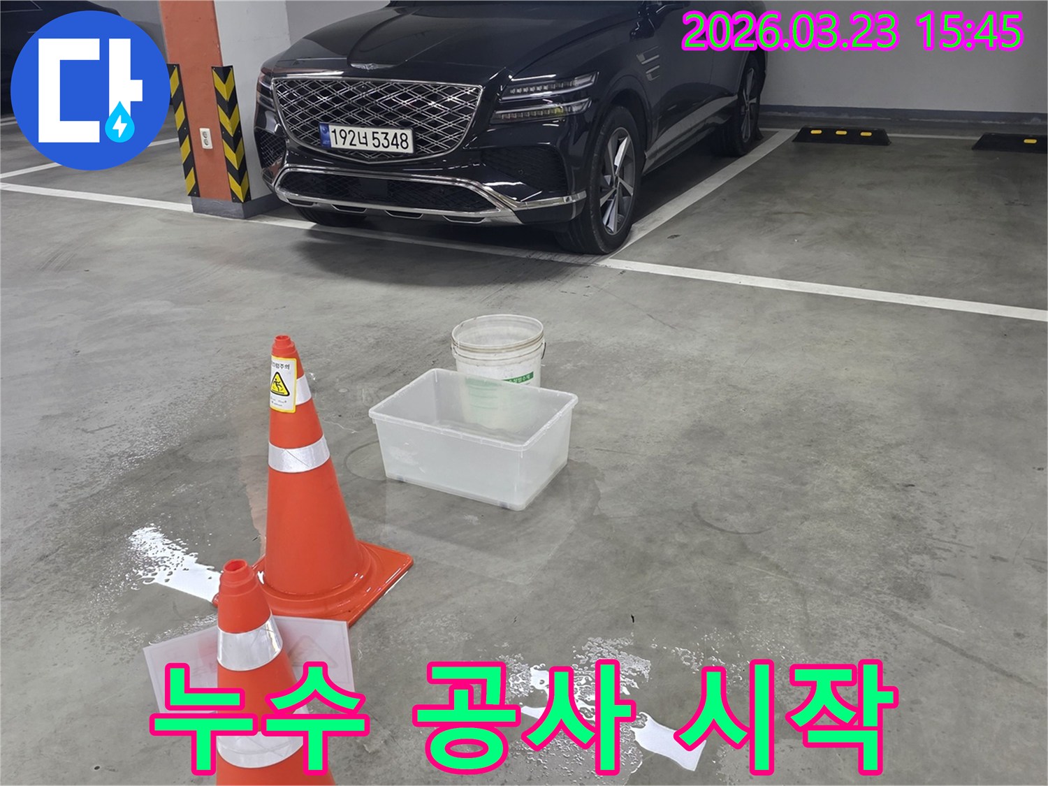 지하주차장 바닥에 물이 고여-안전 콘과 물받이가 놓인-누수 공사 준비 현장입니다.