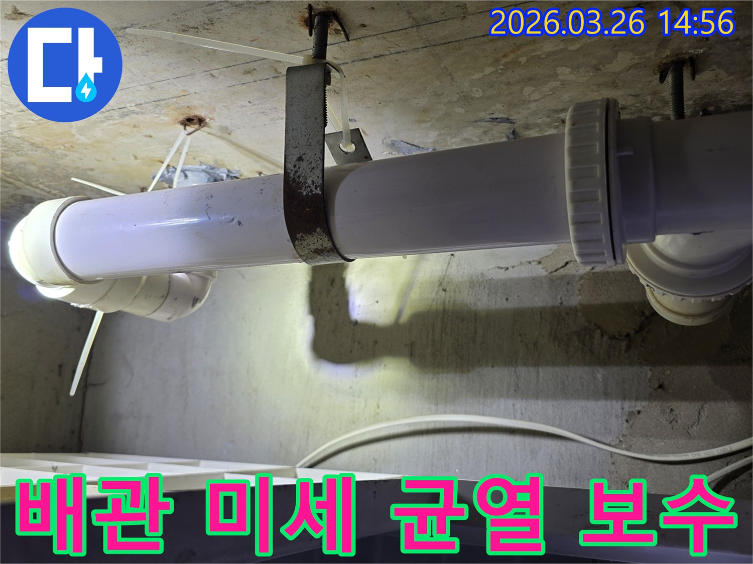 콘크리트 천장 아래에 설치된-하얀색 배관의 표면과-녹슨 지지대 주변을-엔지니어가 면밀히 살피는 모습