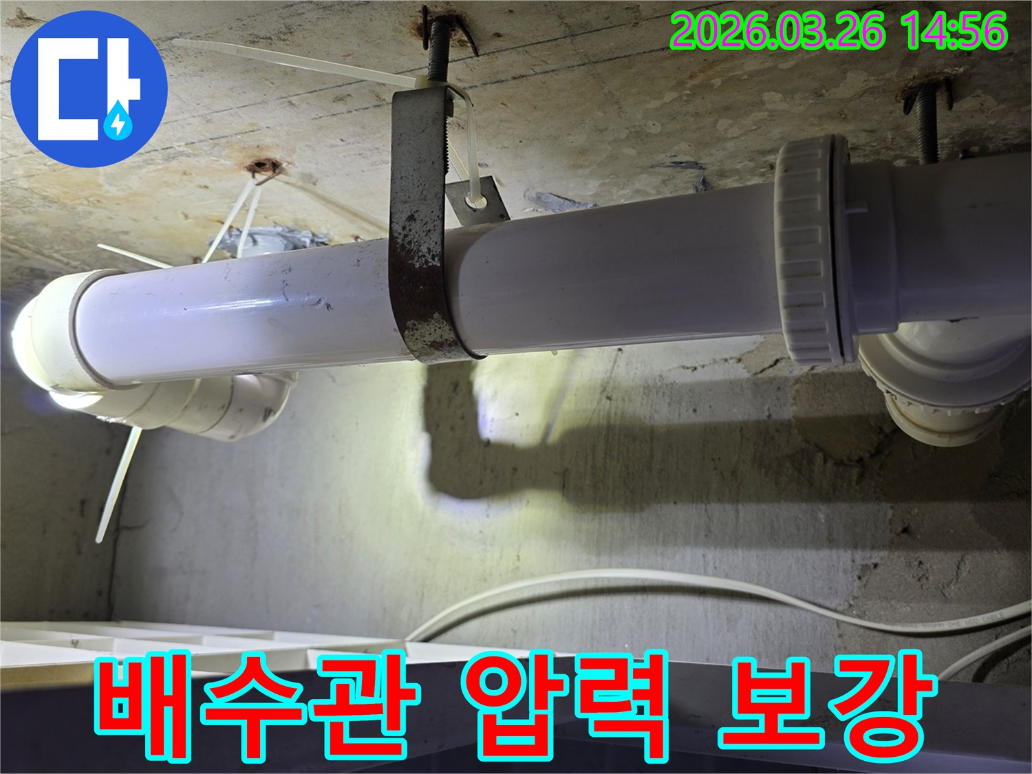 콘크리트 천장에 고정된-하얀색 배수관의 연결 부위와-녹슨 금속 지지대 주변을-엔지니어가 점검하며-압력 테스트를 준비하는 모습