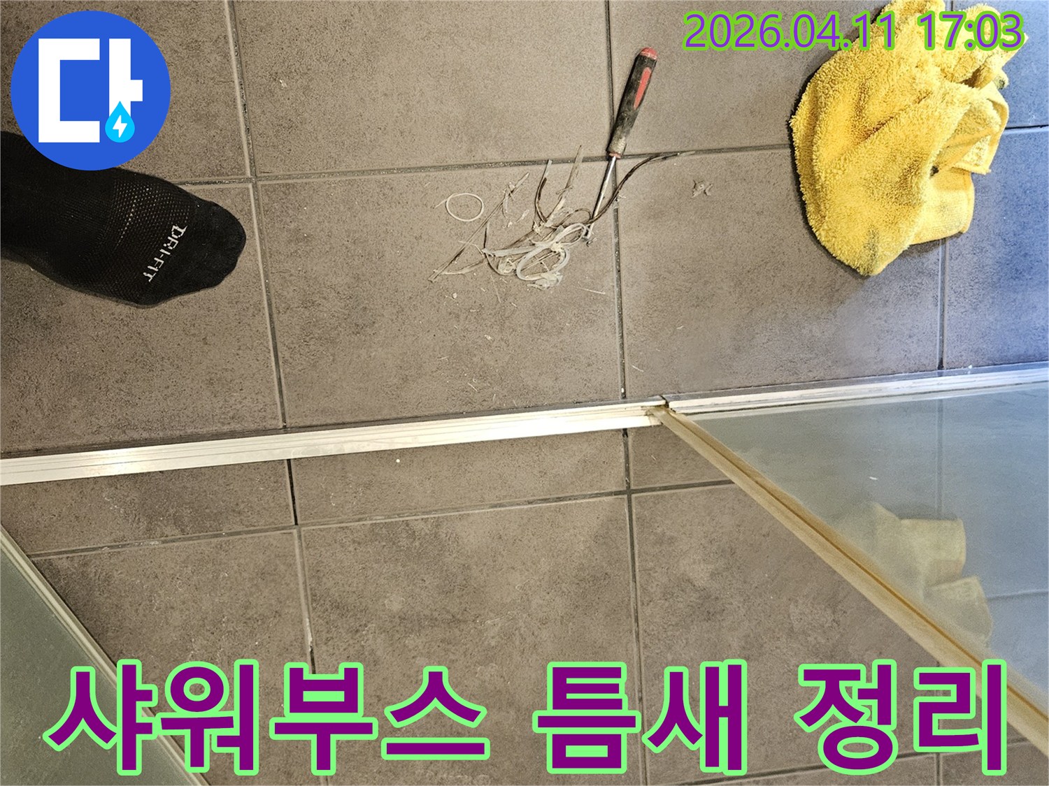 욕실 바닥 타일 위-노란 수건과 공구-그리고 샤워부스 주변의 낡은 실리콘을 제거하는 작업 모습