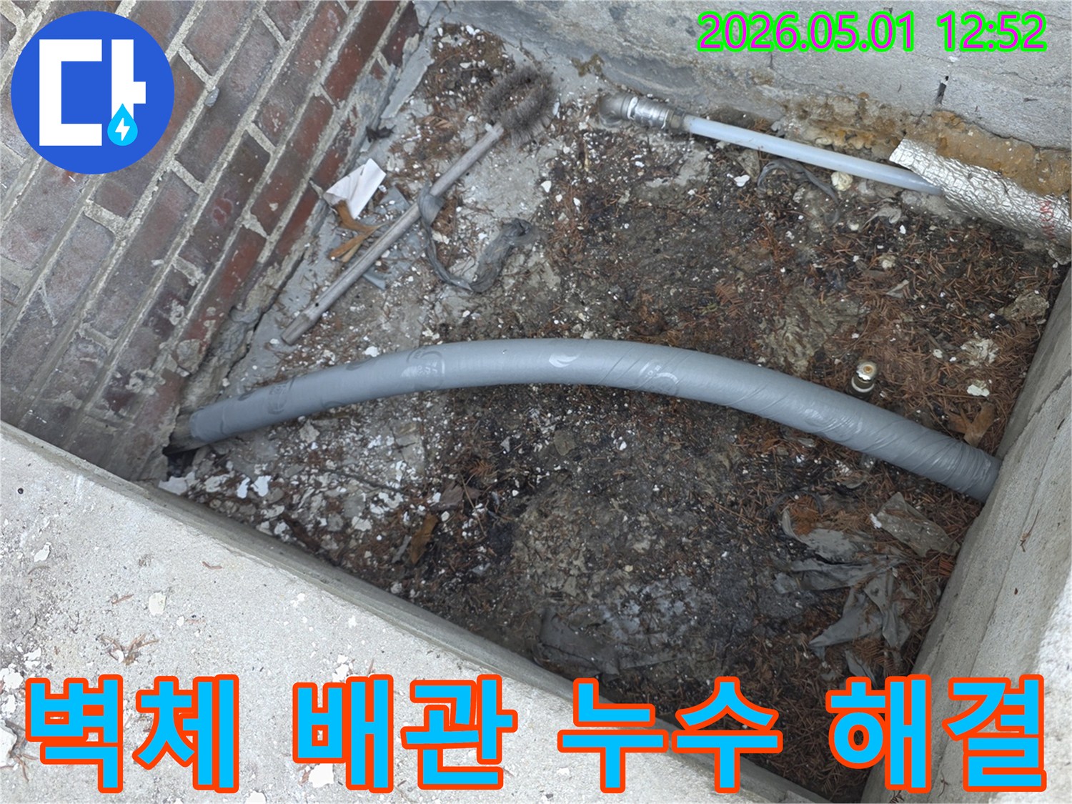 흙과 잔해 속에서-보온 처리된-회색 배관이-새롭게 연결되는-누수 수리 작업의-일부분을 담고 있습니다