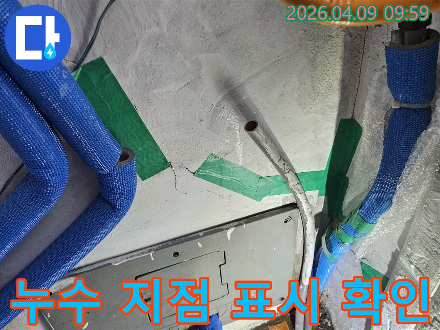 벽면의-콘크리트 균열과-파란색 보온재 배관-그리고 녹색 테이프로-정확히 표시된-누수 발생 지점의-상세한 모습