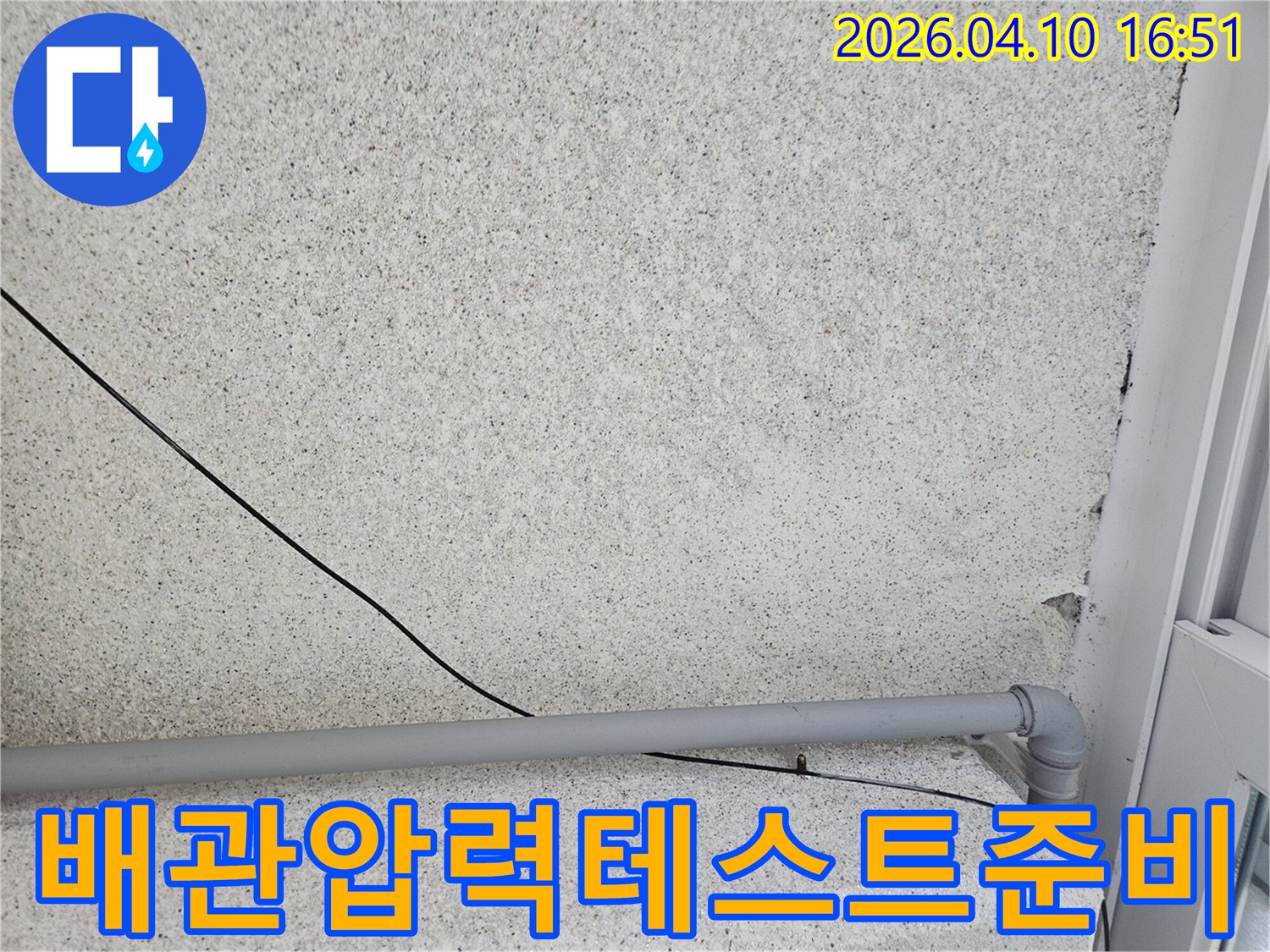 회색 벽에-설치된 회색 배관과-검은 전선이-누수 원인을 찾기 위해-외부 배관의-압력 테스트를-준비하는 모습입니다