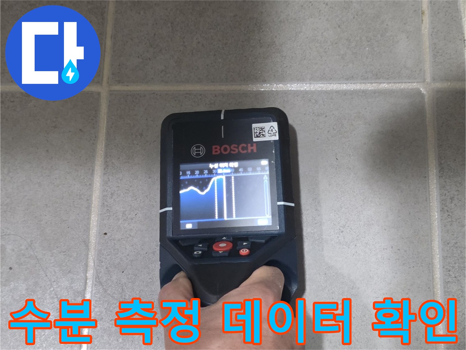 손으로 수분 측정기를 조작하며 타일의 습도를 분석하는 장면
