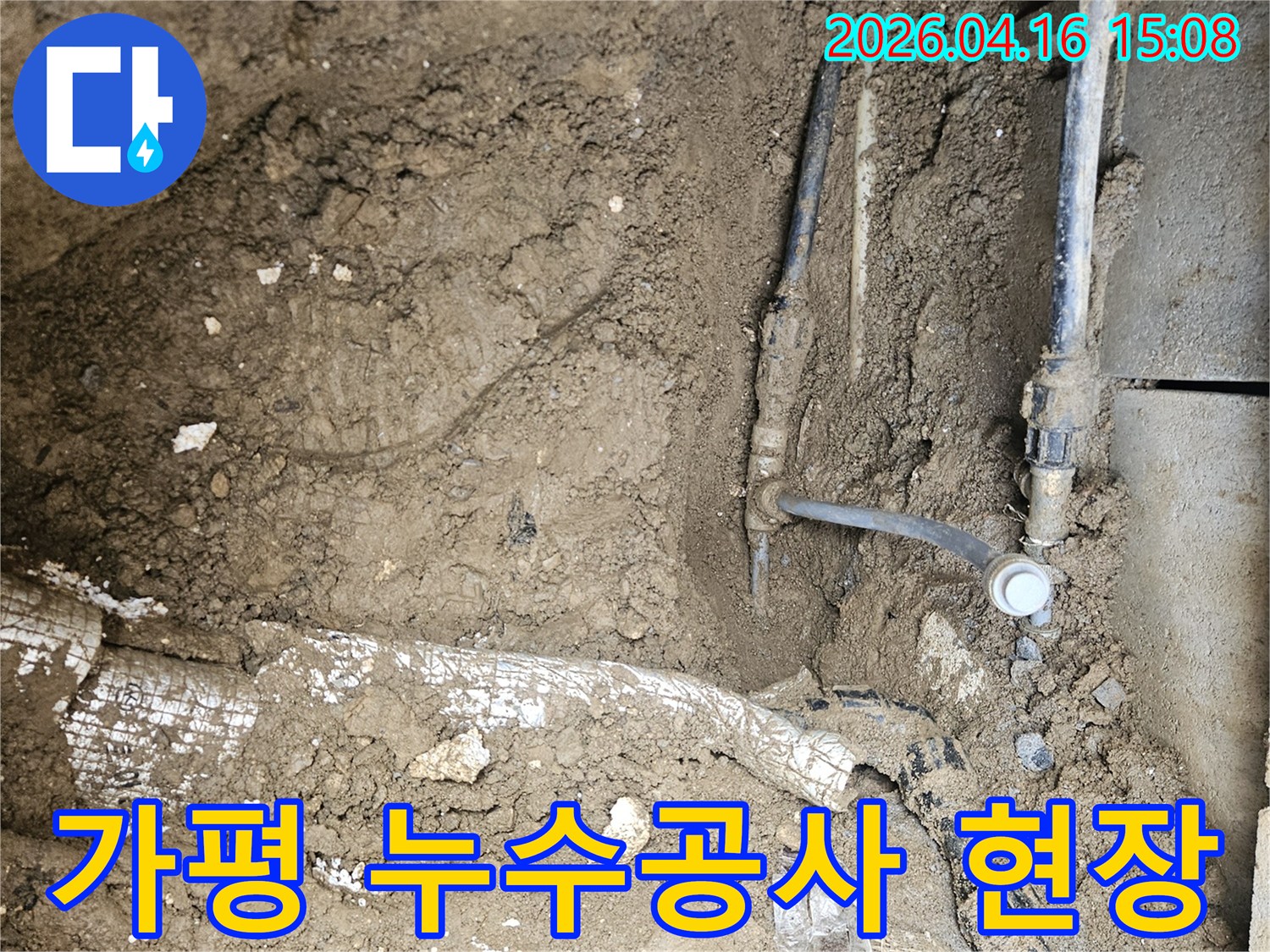 흙을 파내어 드러난 다양한 종류의 배관들 사이에서 누수 지점을 찾아내고 있는 작업 현장입니다.